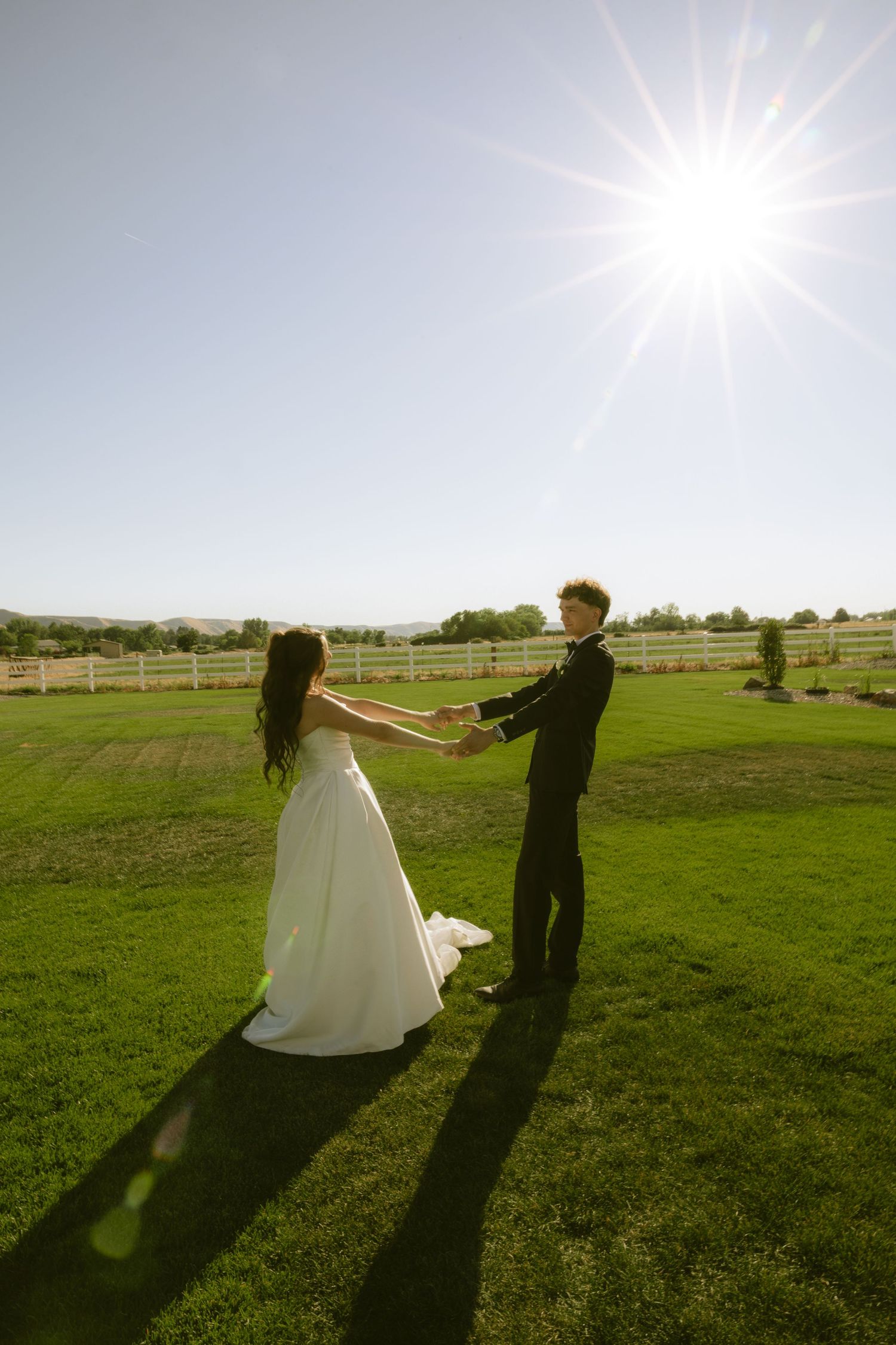 Bride and groom holding hands dancing in sunny green field at outdoor wedding venue.