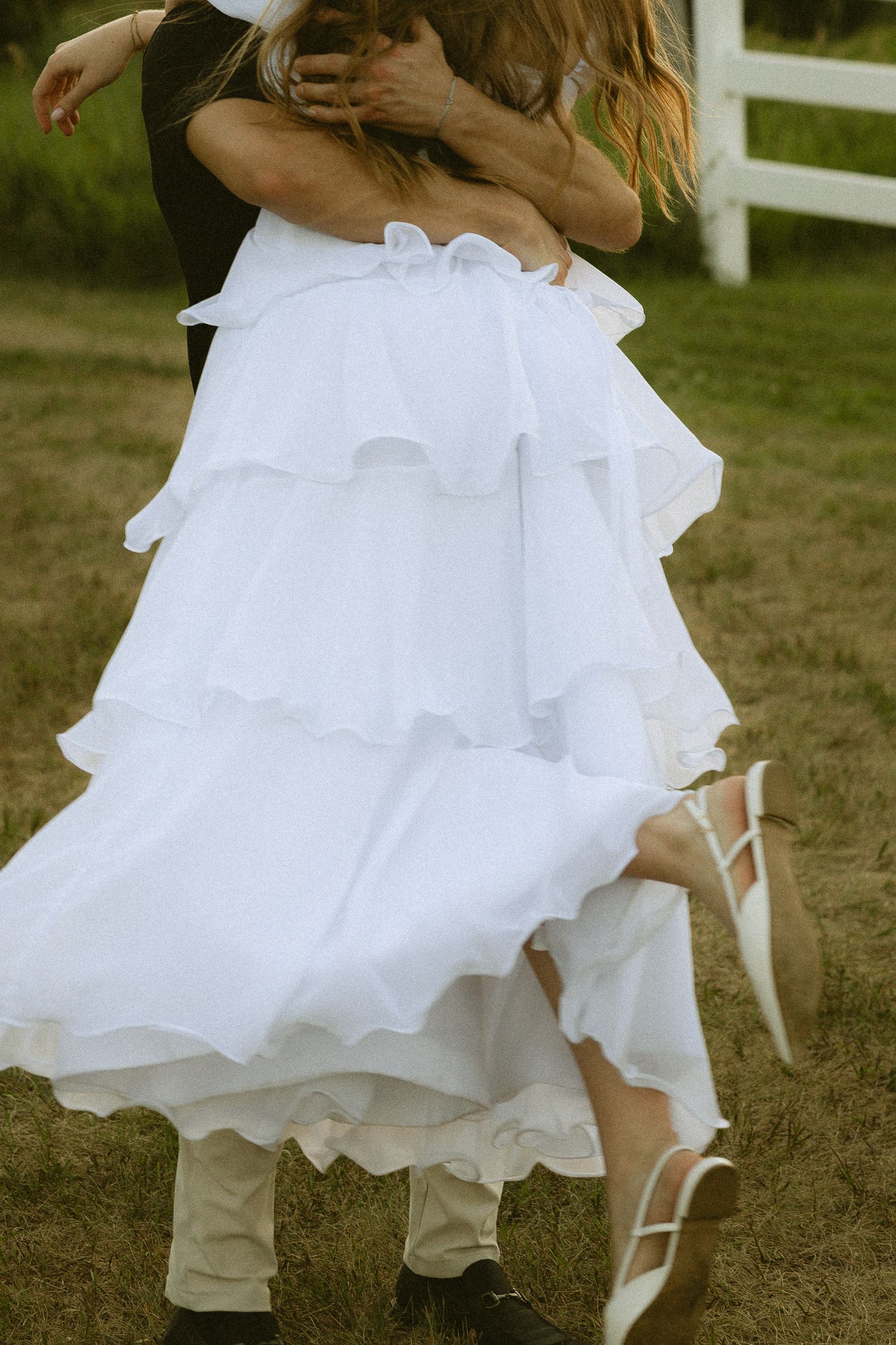 Bride in layered white ruffle wedding dress dancing with groom outdoors on green grass.