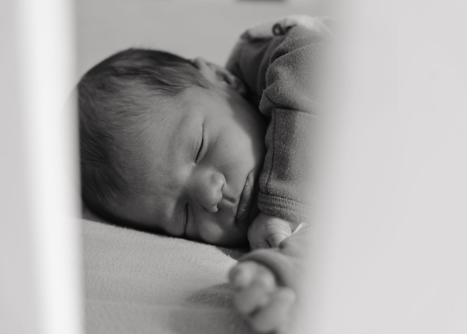 A black and white image of a sleeping newborn baby, curled up and resting peacefully.