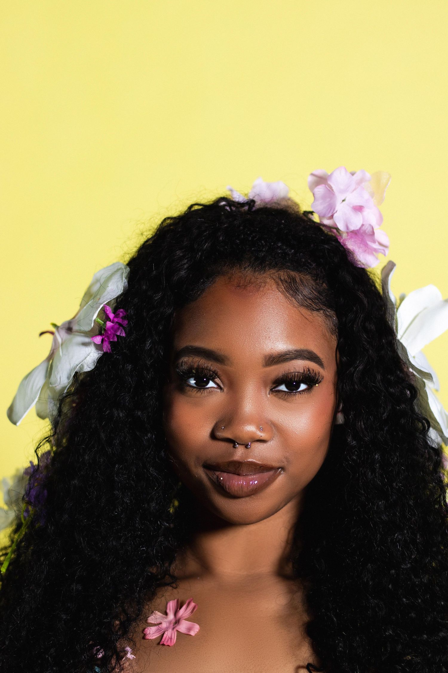 Portrait of woman with flowers in curly hair on yellow background.