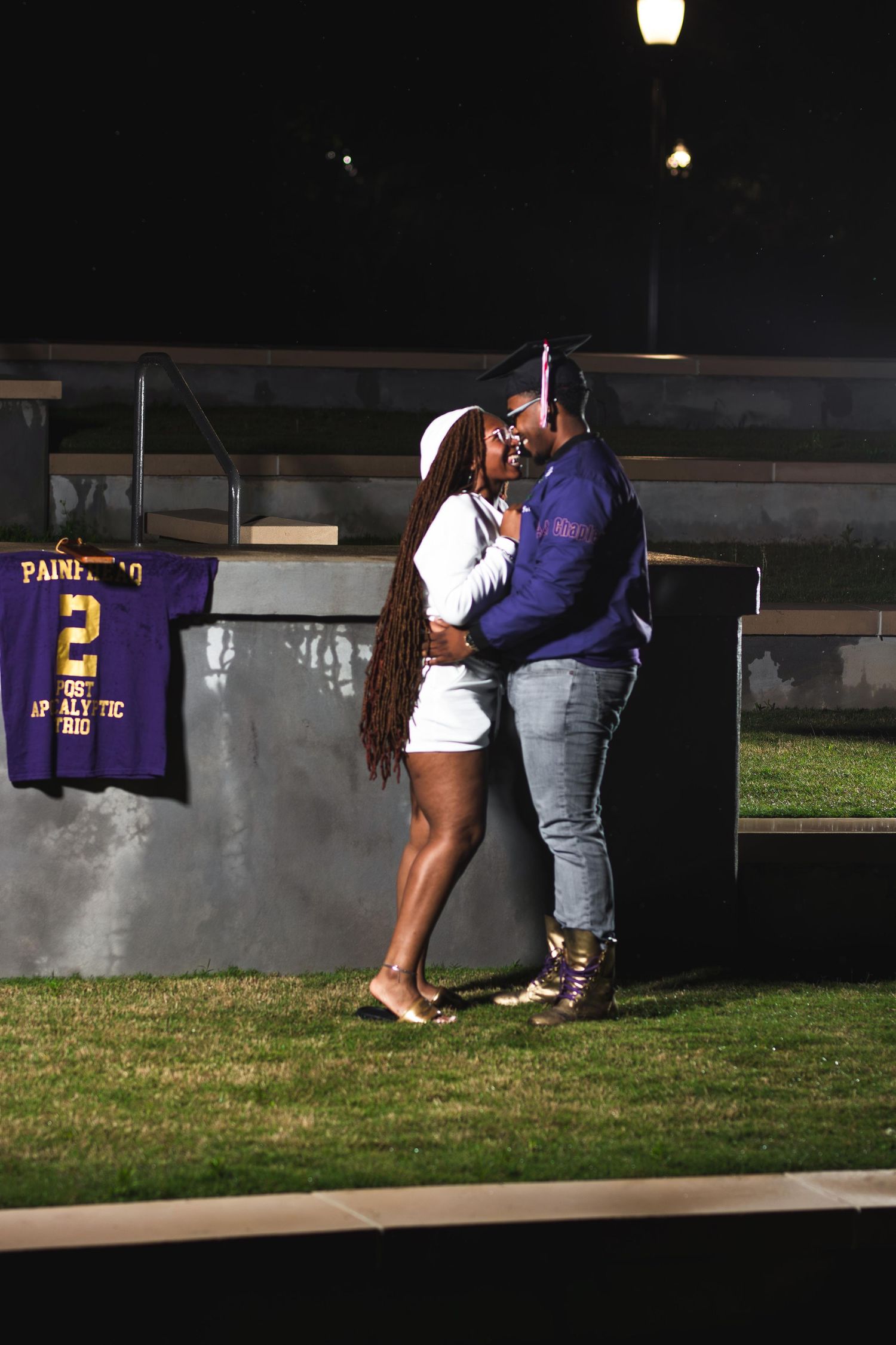 Two people share an intimate moment at night outdoors near a purple jersey hanging on a wall.