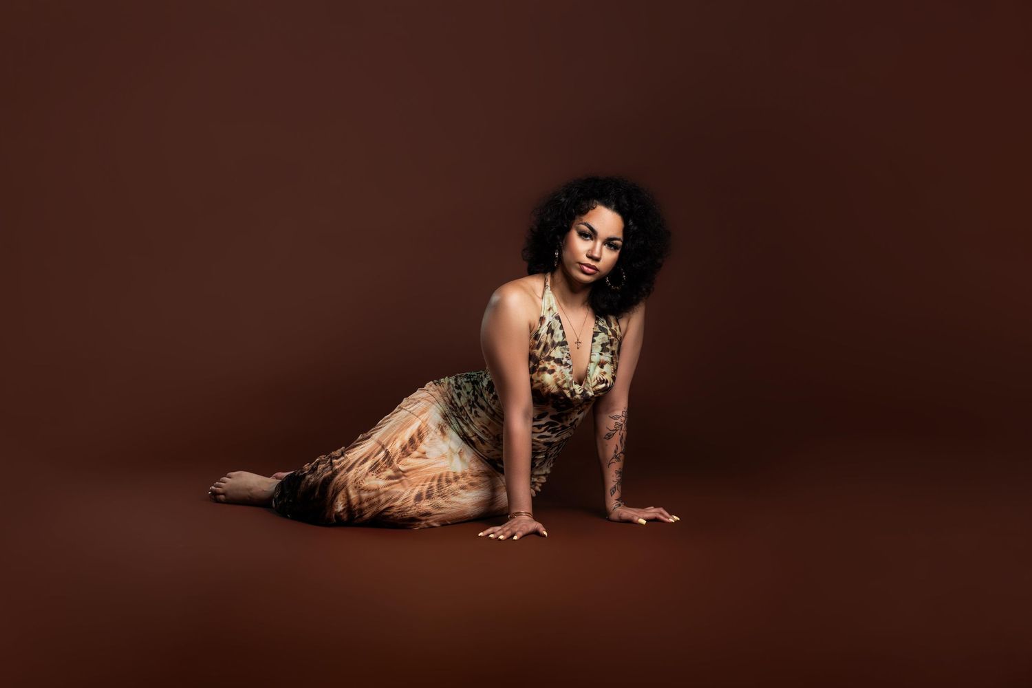 Woman in floral halter dress poses gracefully on floor against warm brown studio background.