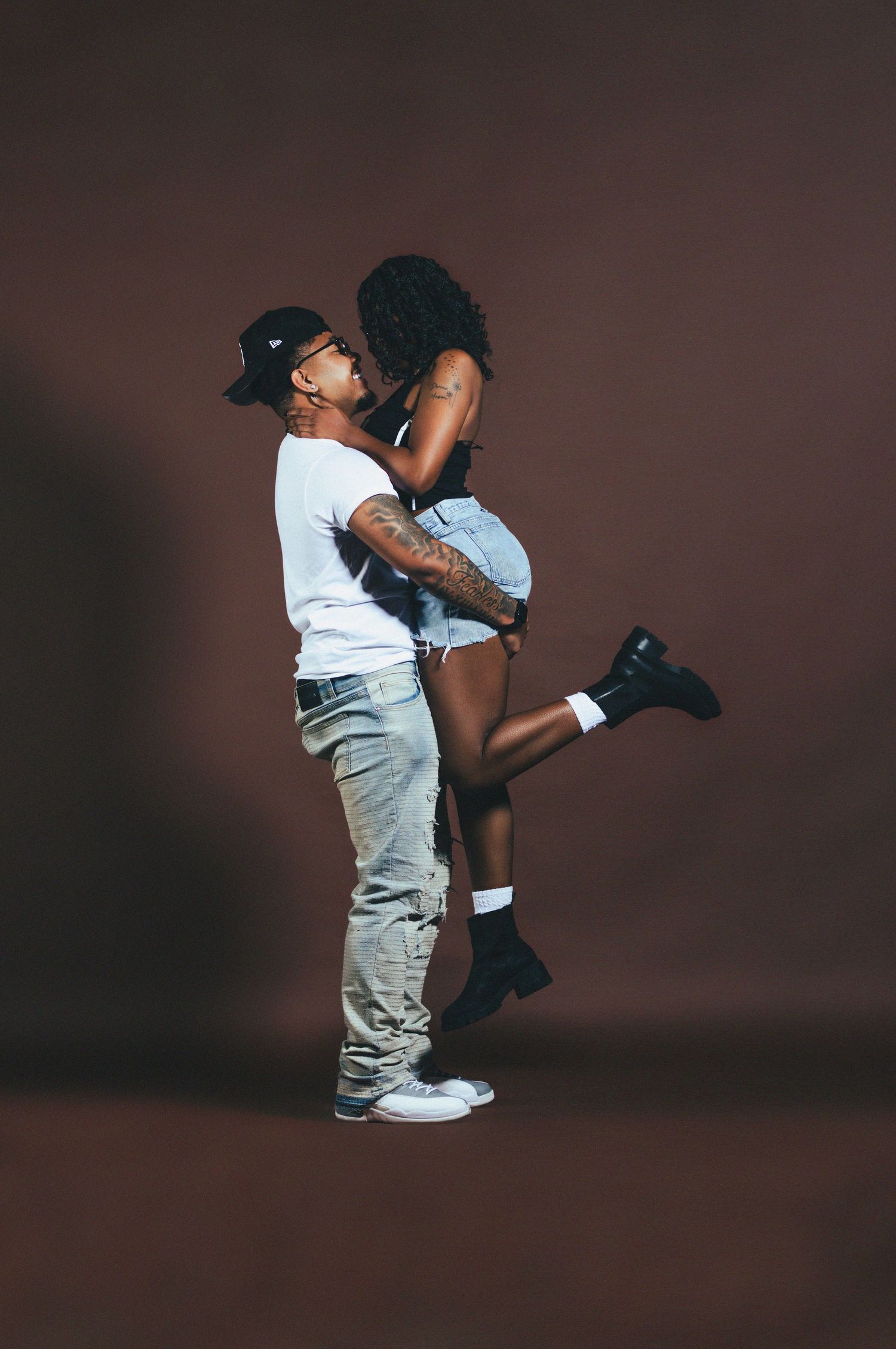Couple sharing a romantic moment, man lifting woman in a studio with a dark brown background.