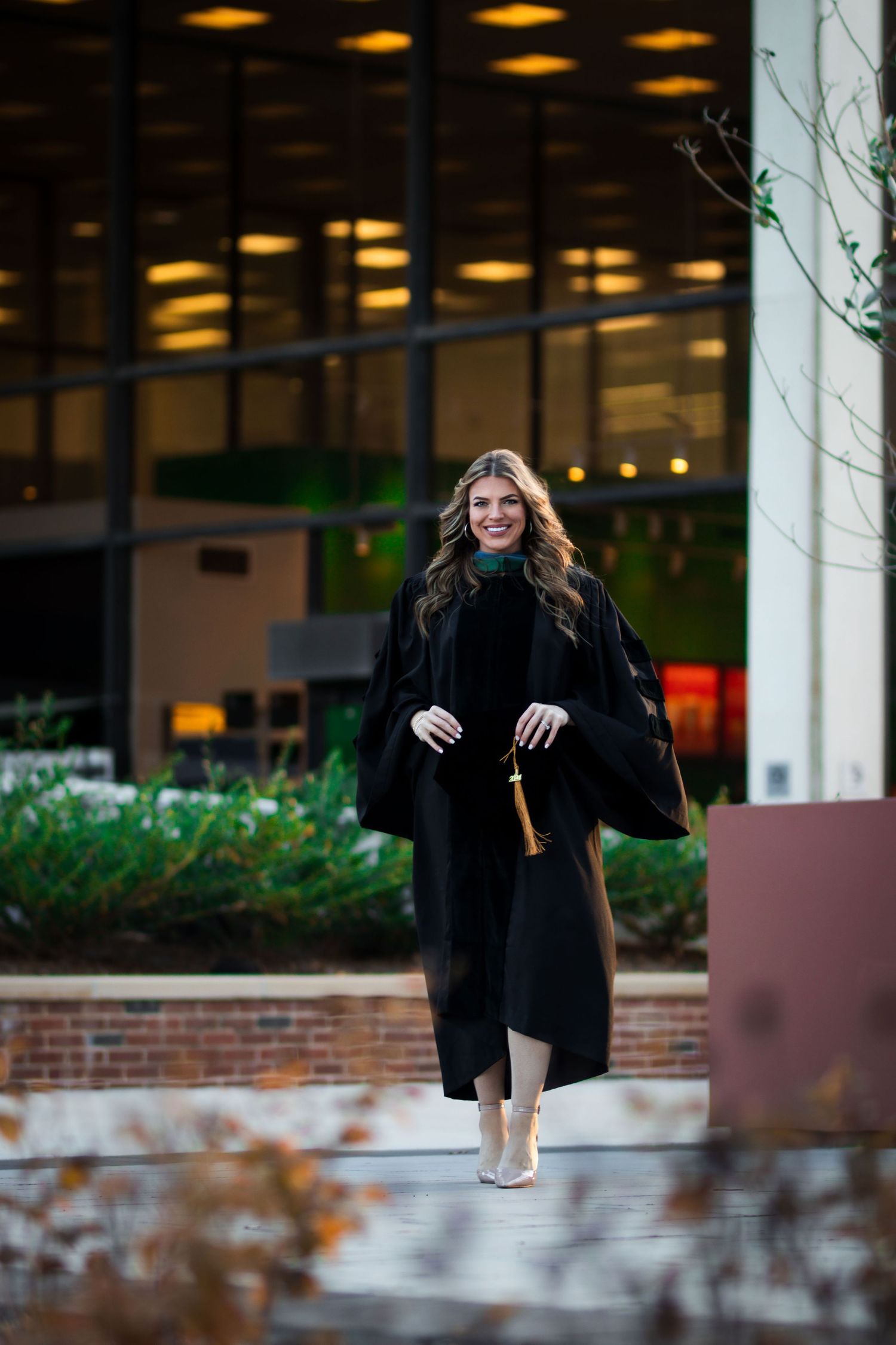 Smiling female graduate in black doctoral regalia walks outside university building.