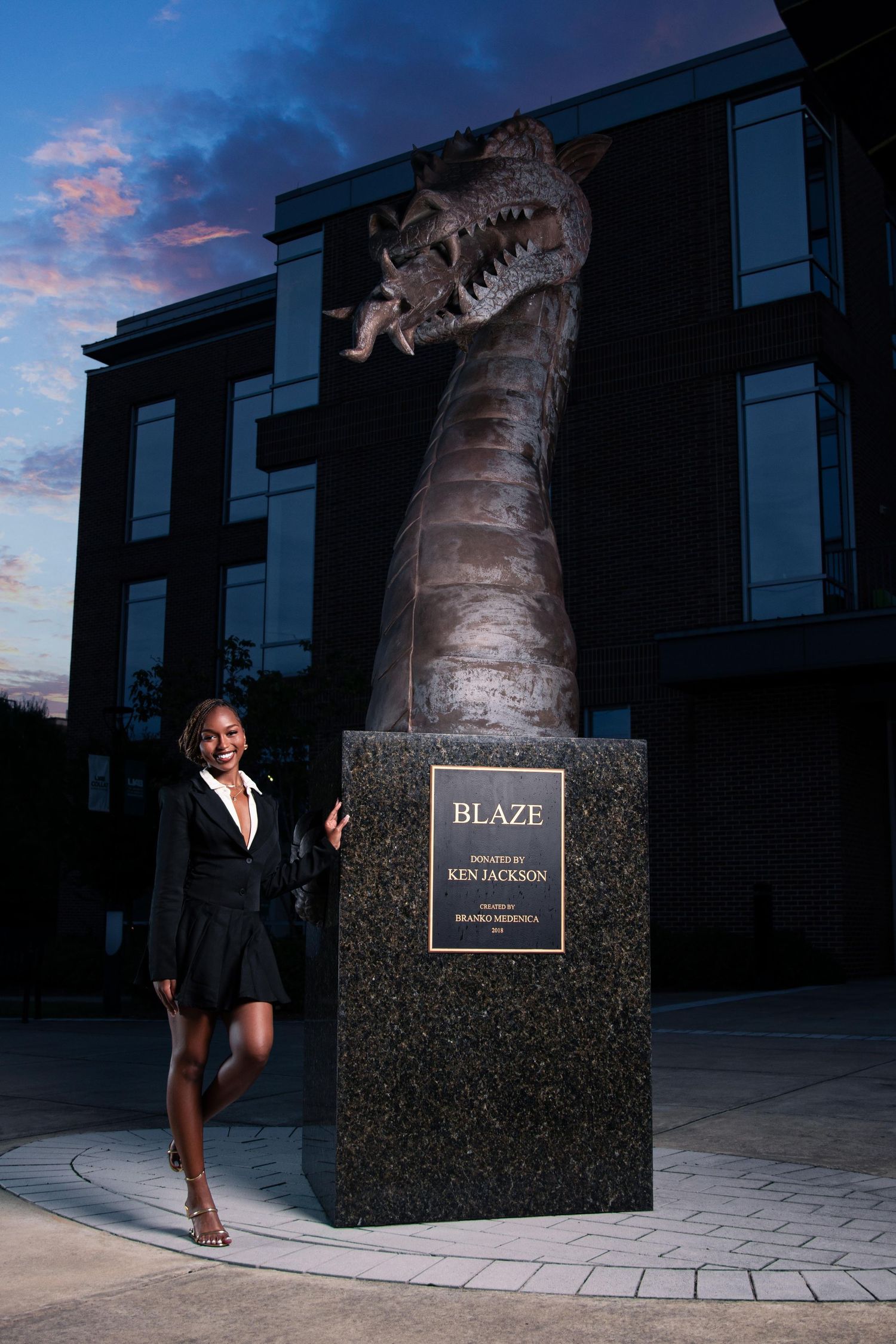 Woman posing beside the Blaze dragon statue sponsored by Ken Jackson at dusk.