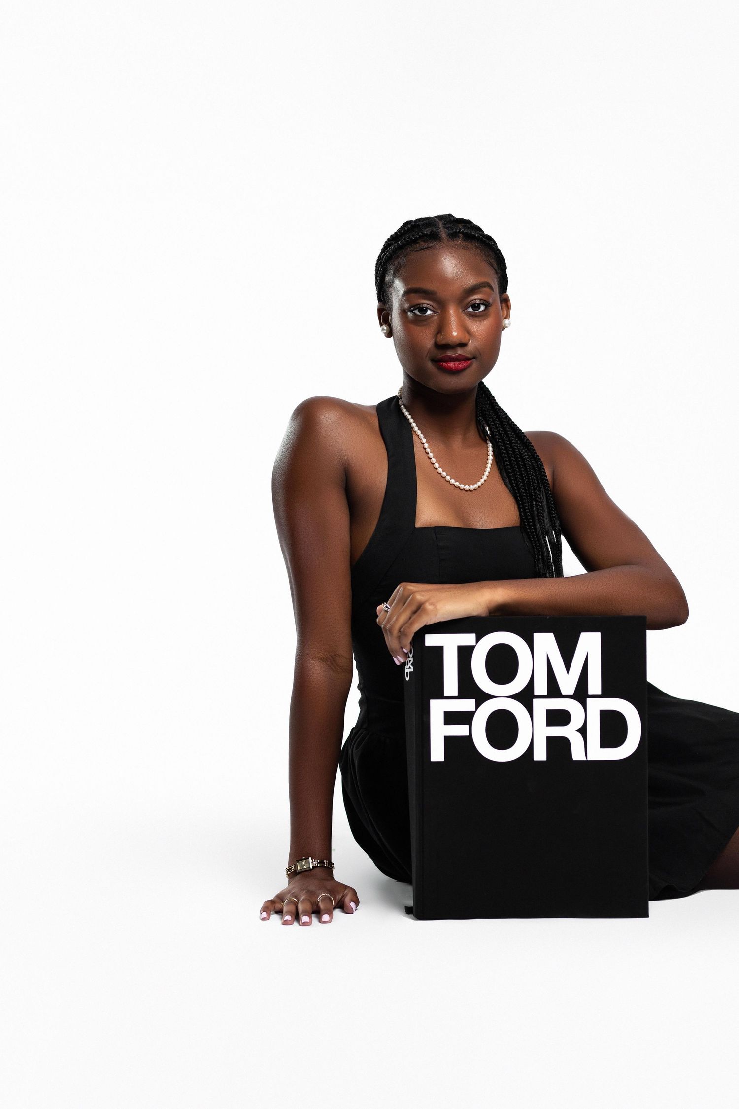 A Black woman in black dress sits holding a Tom Ford book against white background.