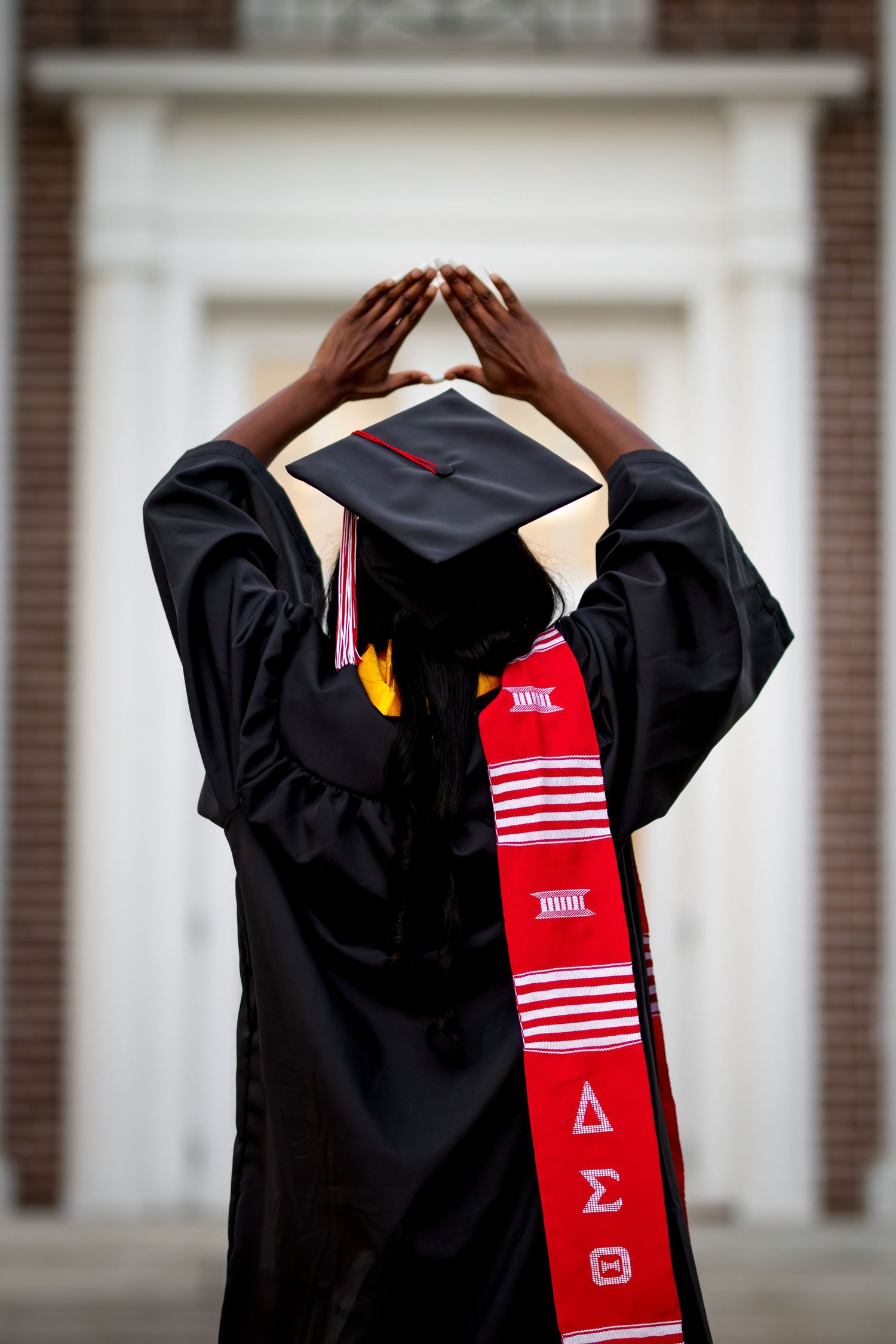 Graduate in black cap and gown with Delta Sigma Theta stole forms hand sign behind head.