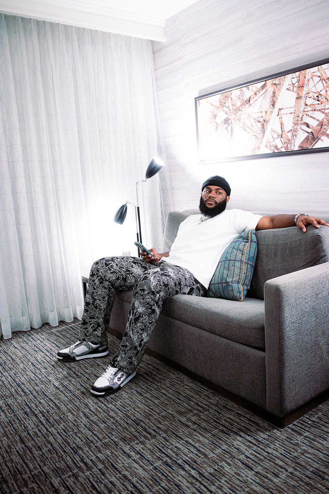 Bearded man in patterned pants relaxing on gray sofa in modern hotel room.