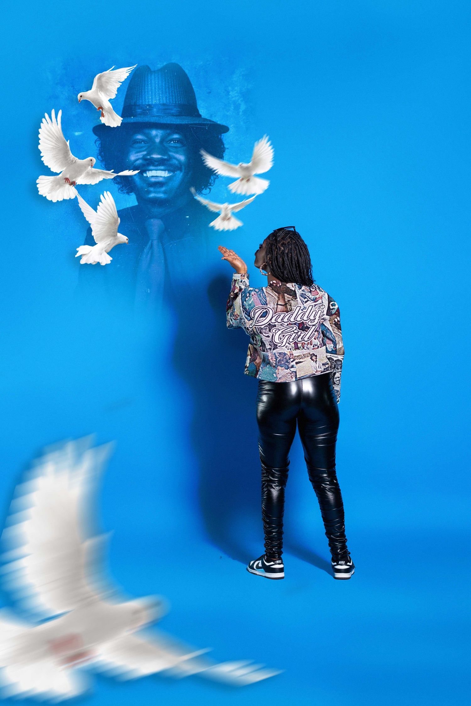 Person releasing white doves toward a glowing portrait on a blue background in a studio photo.