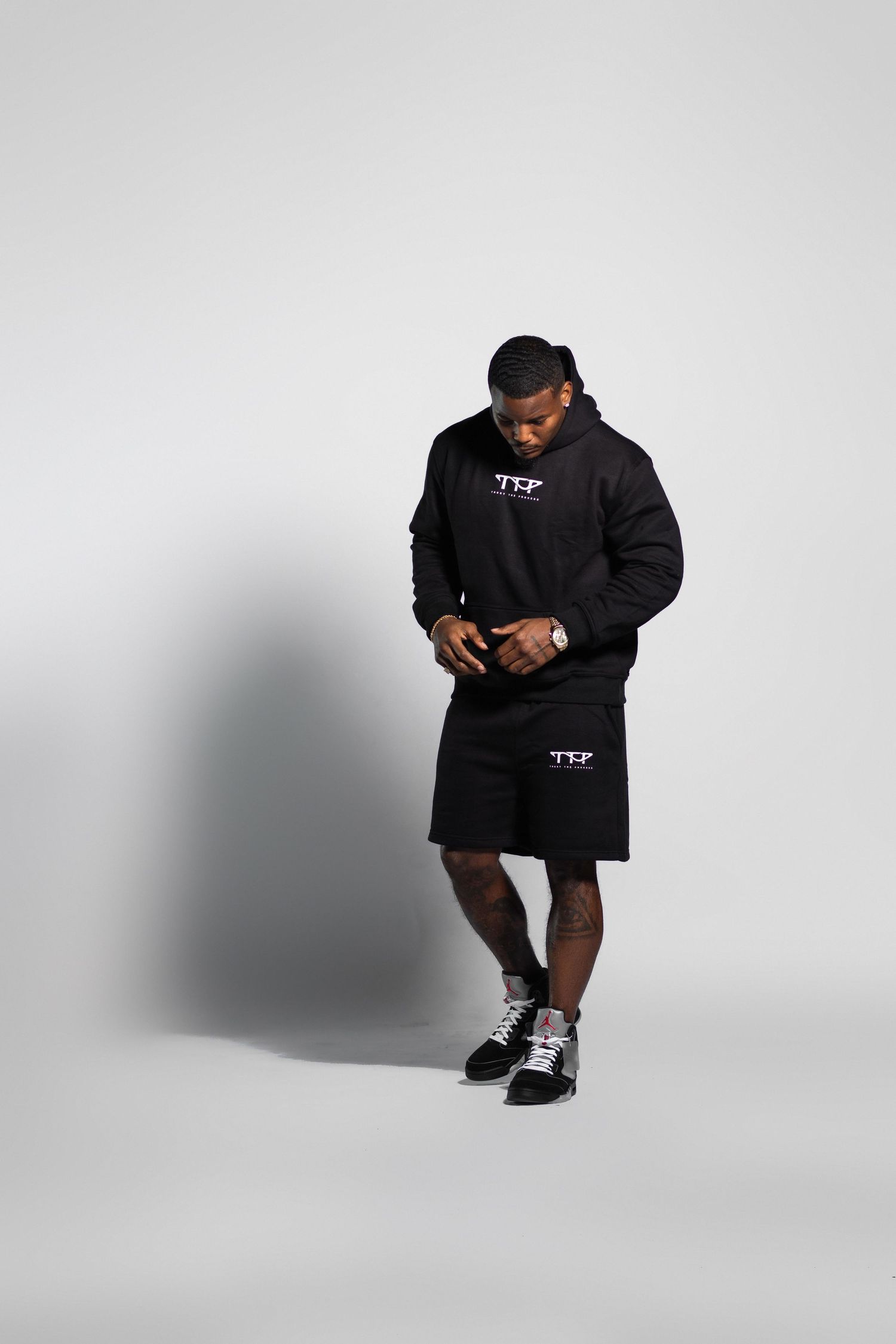 Man in black hoodie and shorts streetwear set on white background.