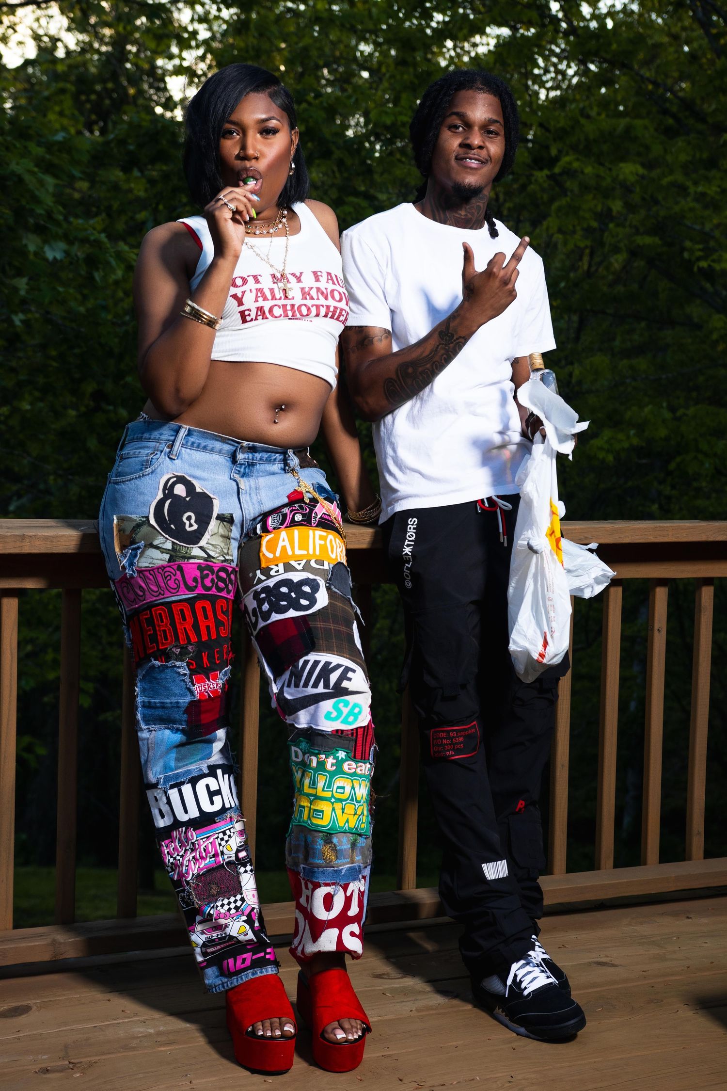 Young Black couple posing on a deck, woman in patchwork jeans and man in white t-shirt with black pants.
