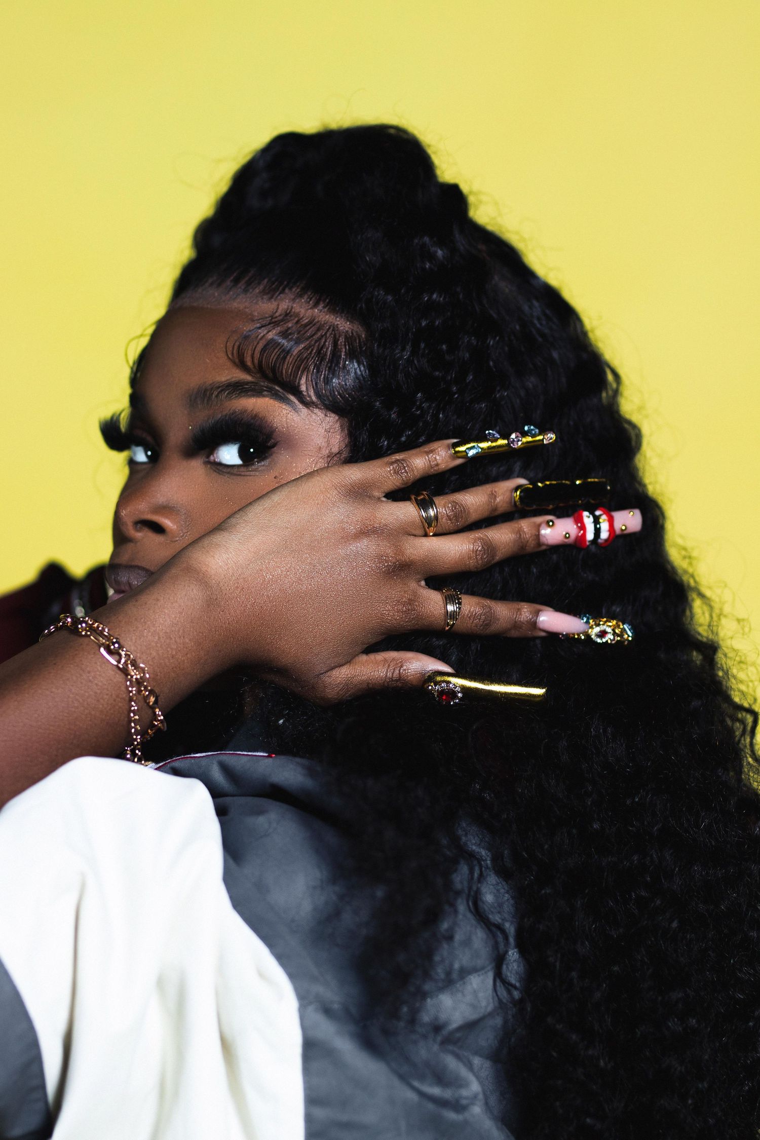Woman with long decorated nails and curly ponytail against yellow background.