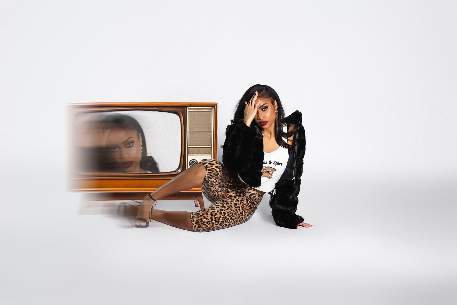 Woman in leopard print pants and black hoodie poses beside a vintage television set.
