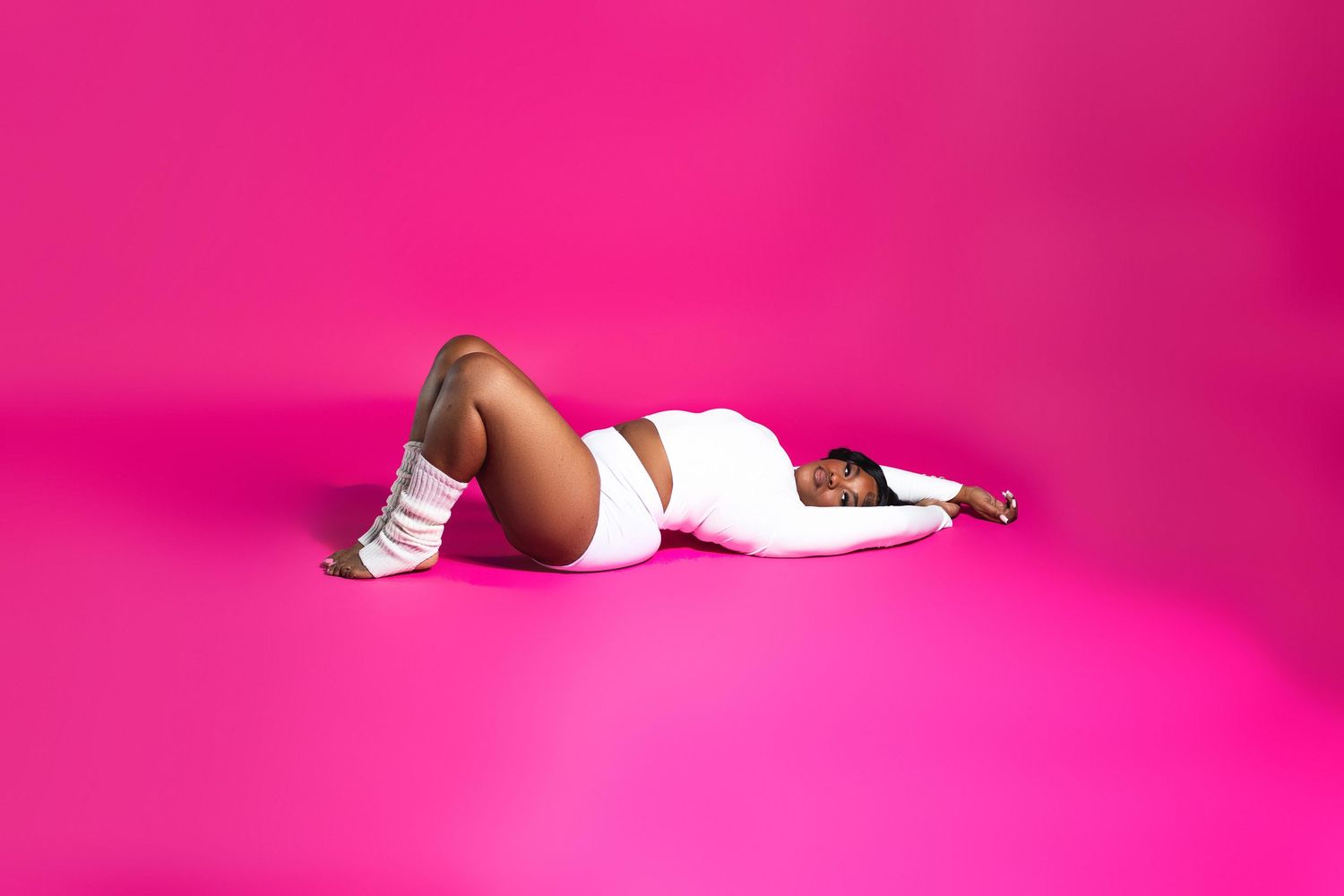 Woman in white bodysuit lying on hot pink studio floor.