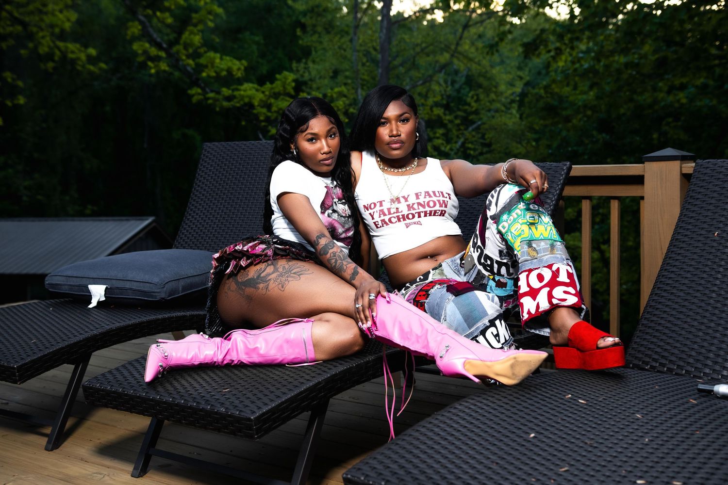 Two Black women in matching white tops and pink boots relaxing together on lounge chairs on an outdoor deck.