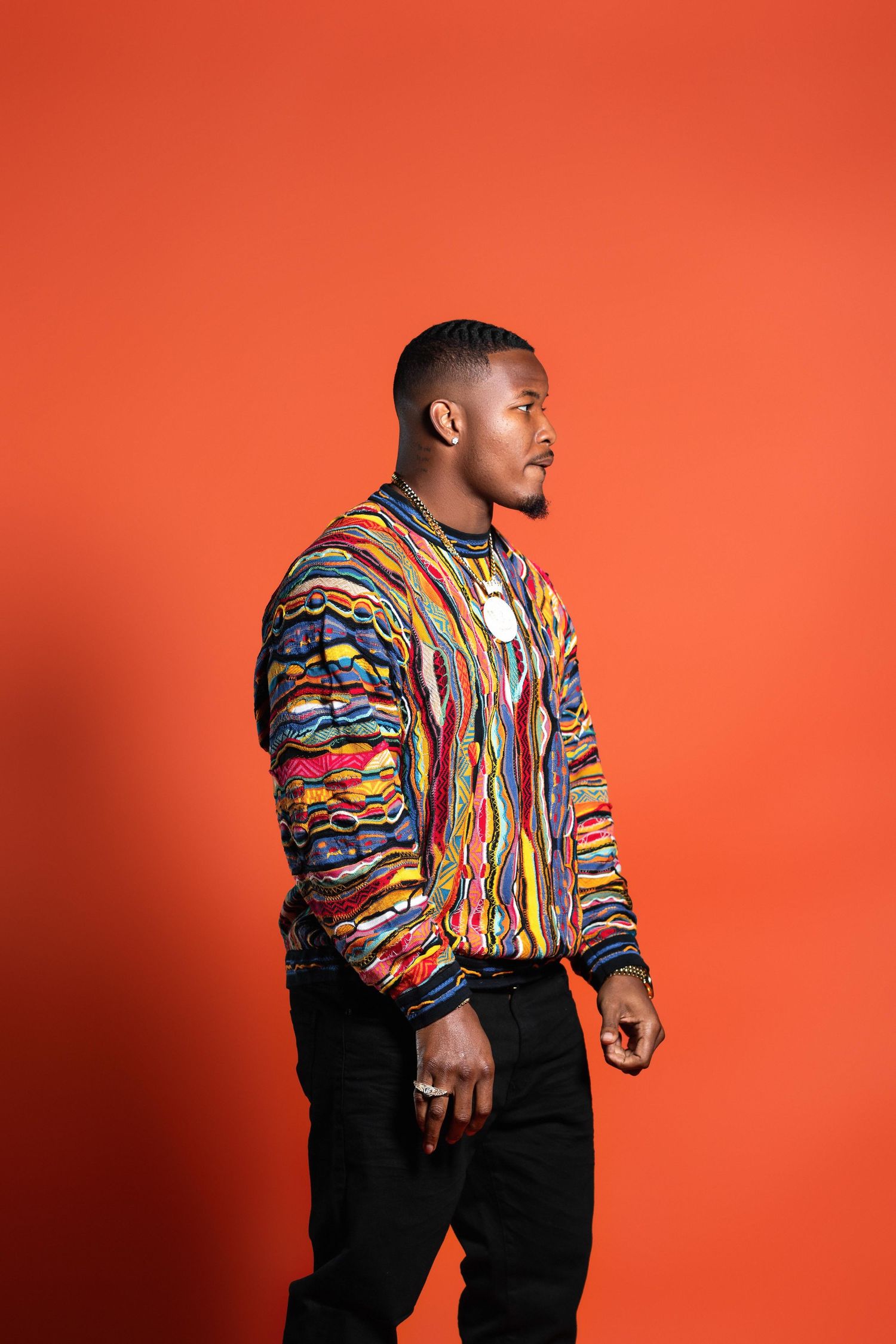 Man in multicolor striped bomber jacket posing on orange background.