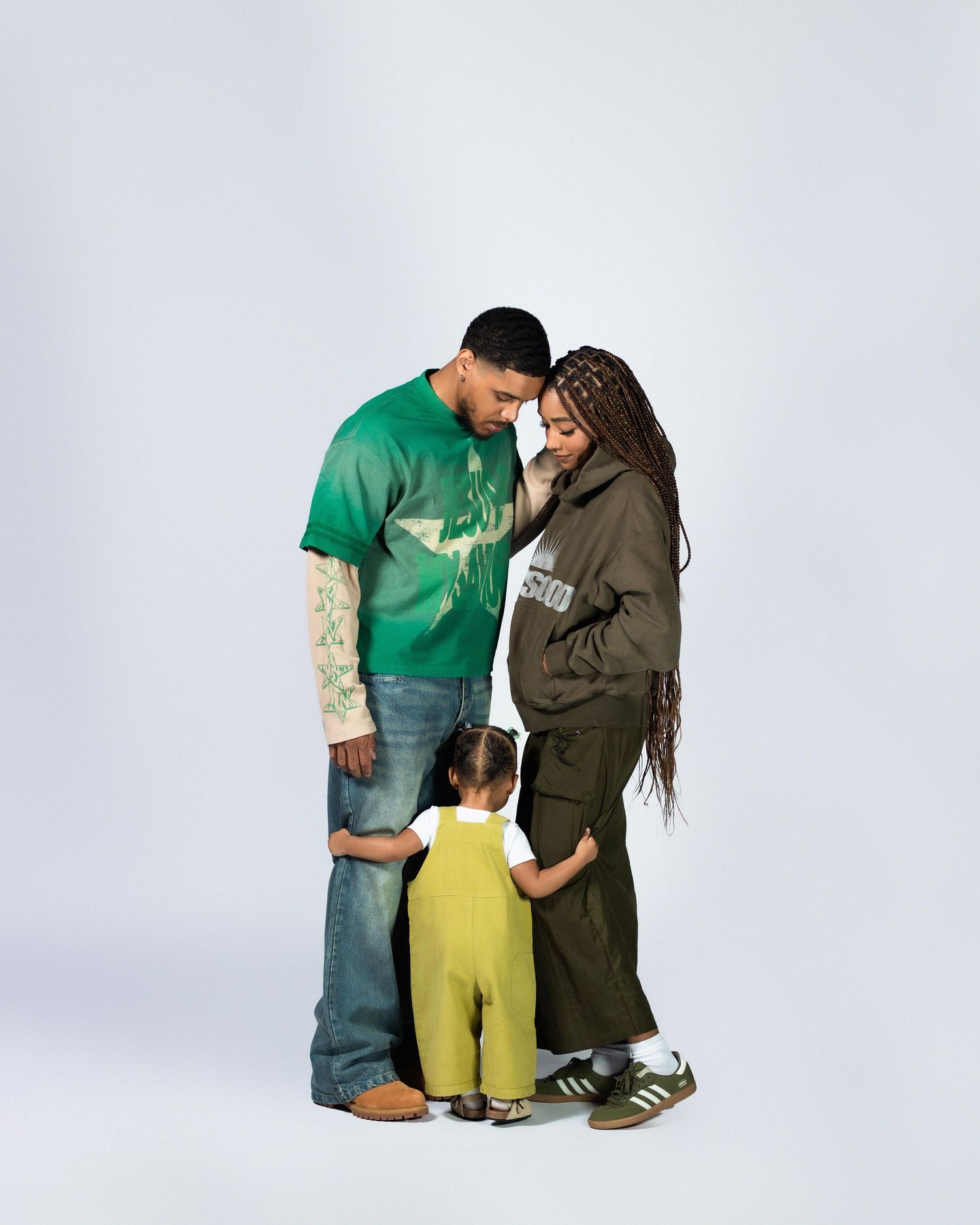 Family of three in coordinated green outfits posing on white background.