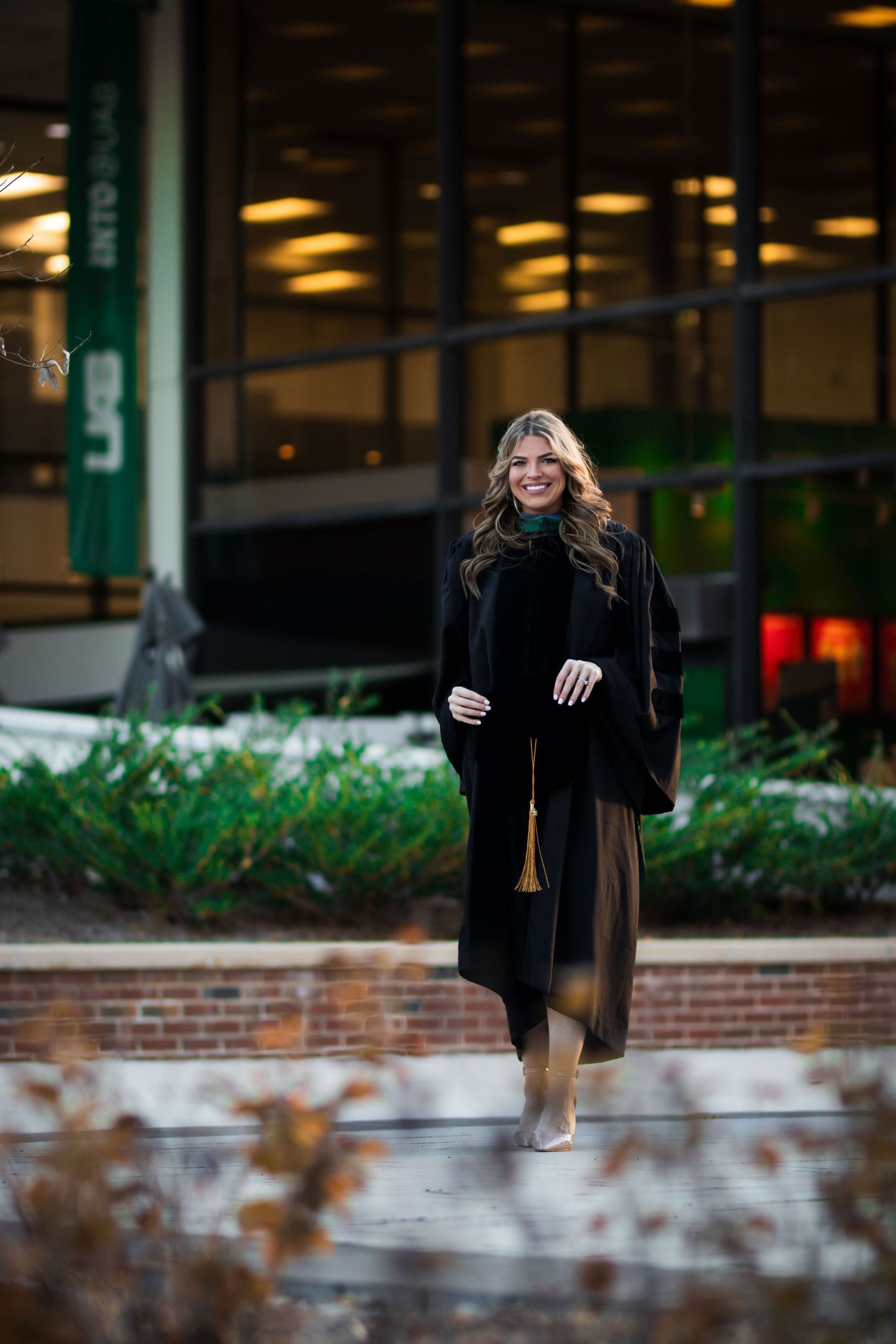 Smiling graduate in black cap and gown posing in front of a UAB university building exterior.