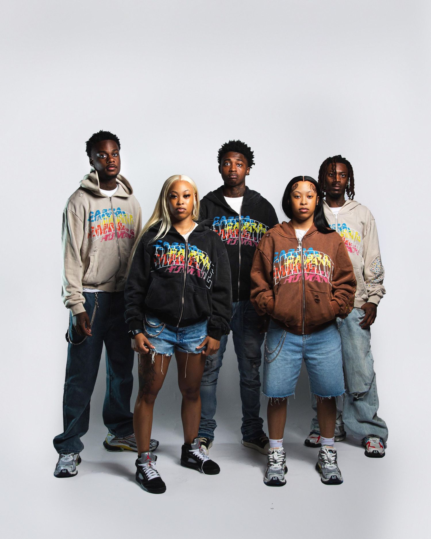 Five young people posing in matching colorful graphic hoodies and casual streetwear against a white background.