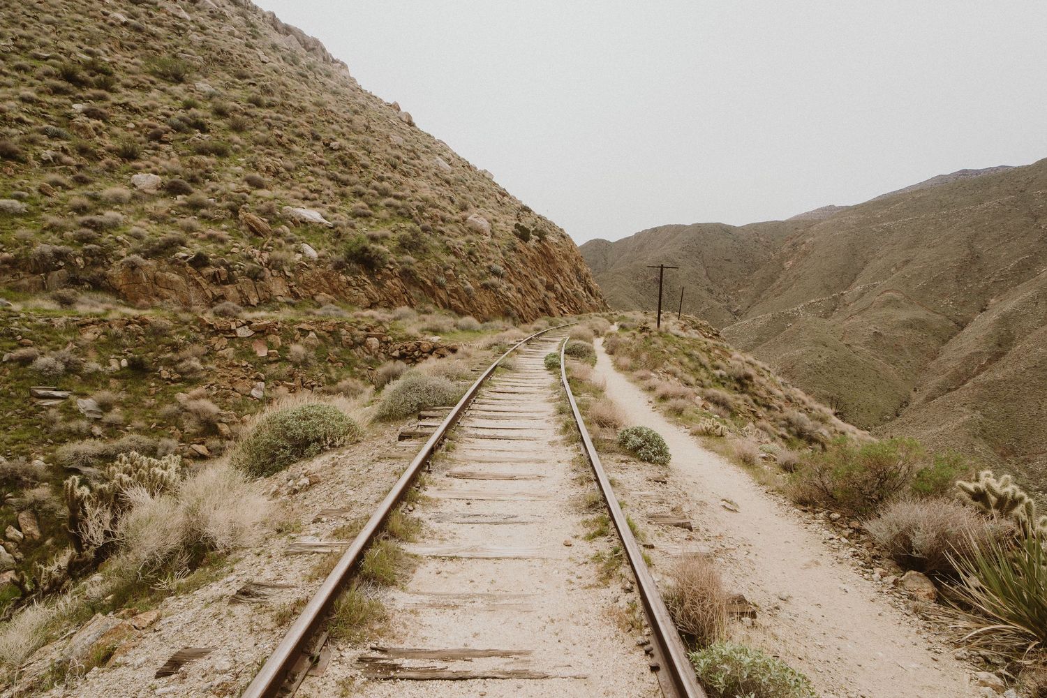 A scenic mountain railway track curves through rugged terrain with rocky slopes and sparse vegetation.
