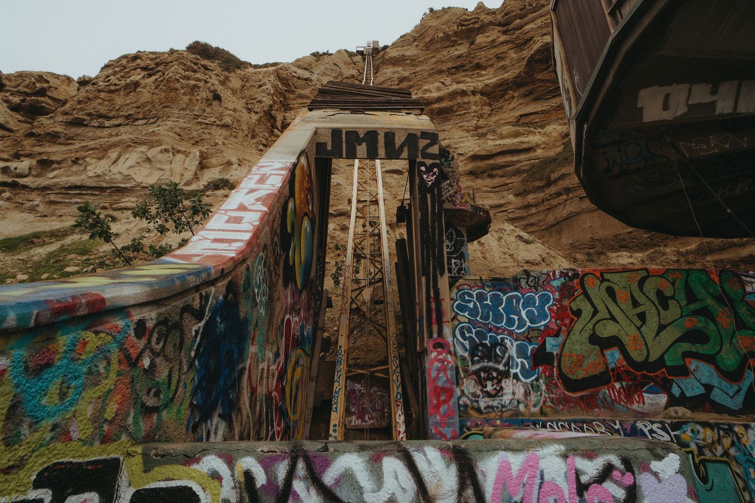 Graffiti-covered concrete walls beneath rocky cliffs create an urban contrast against the natural desert landscape.