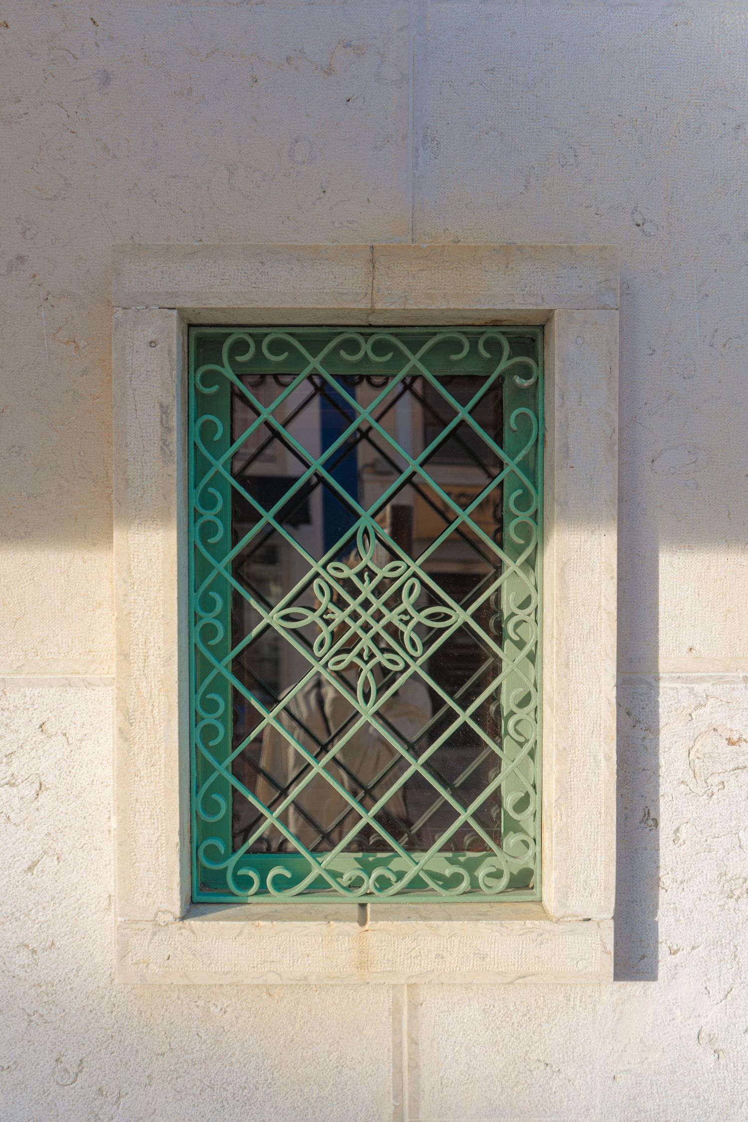 Four matching white stone basement windows with decorative green metal grilles in a geometric pattern.