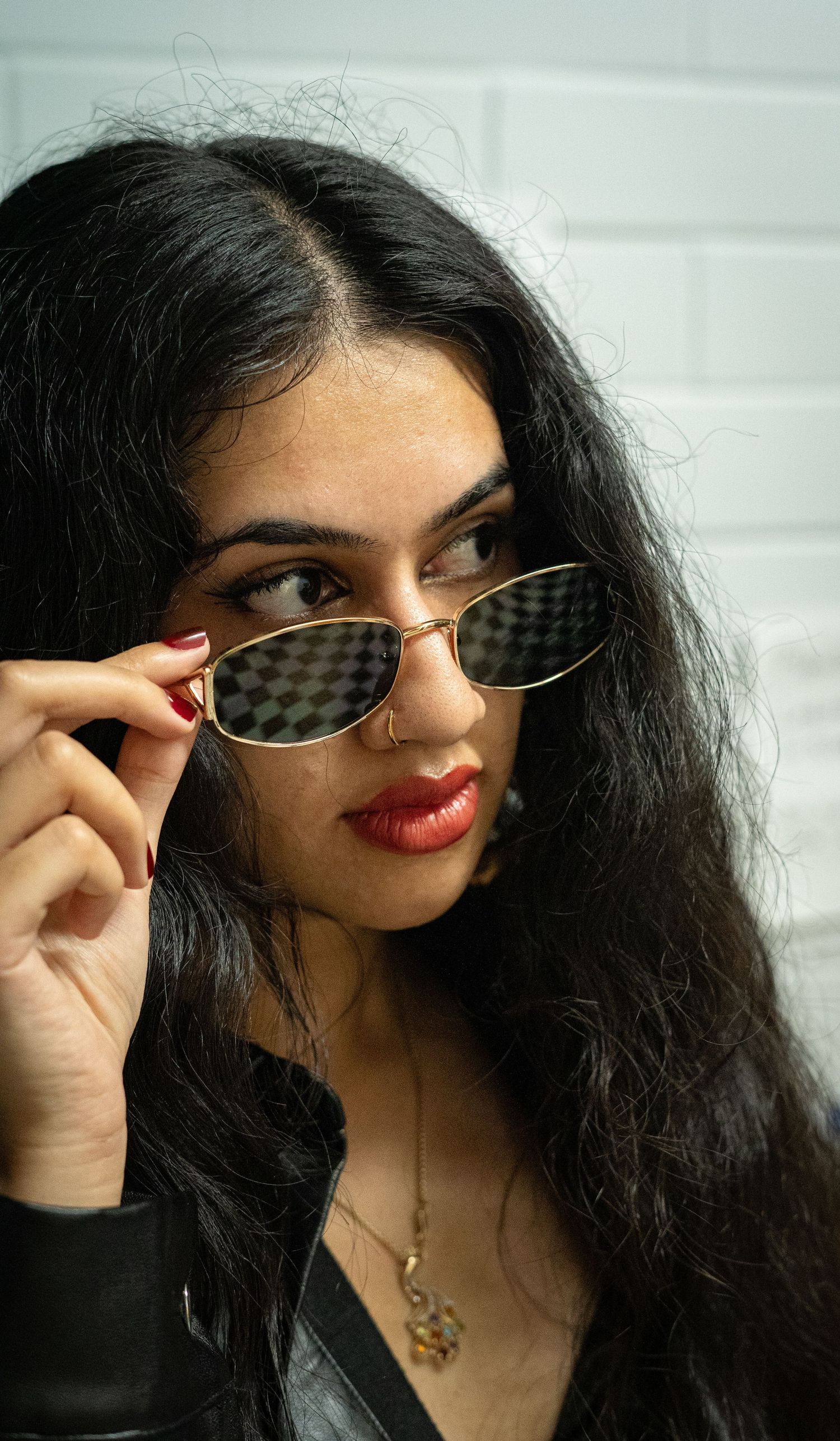 Stylish individual wearing checkered sunglasses and dark lipstick against white background.