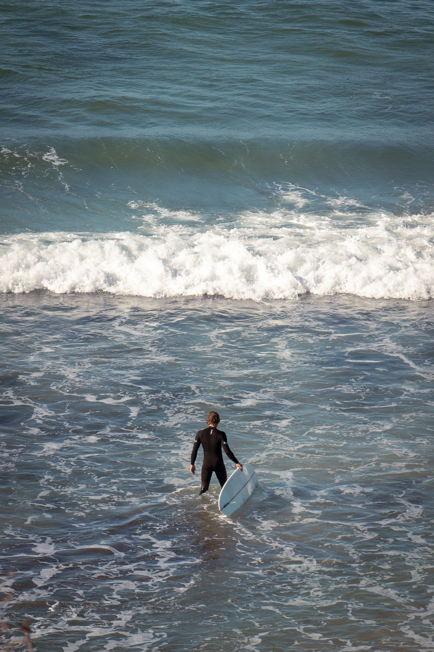 Surfers walking into crashing ocean waves on a sunny day.