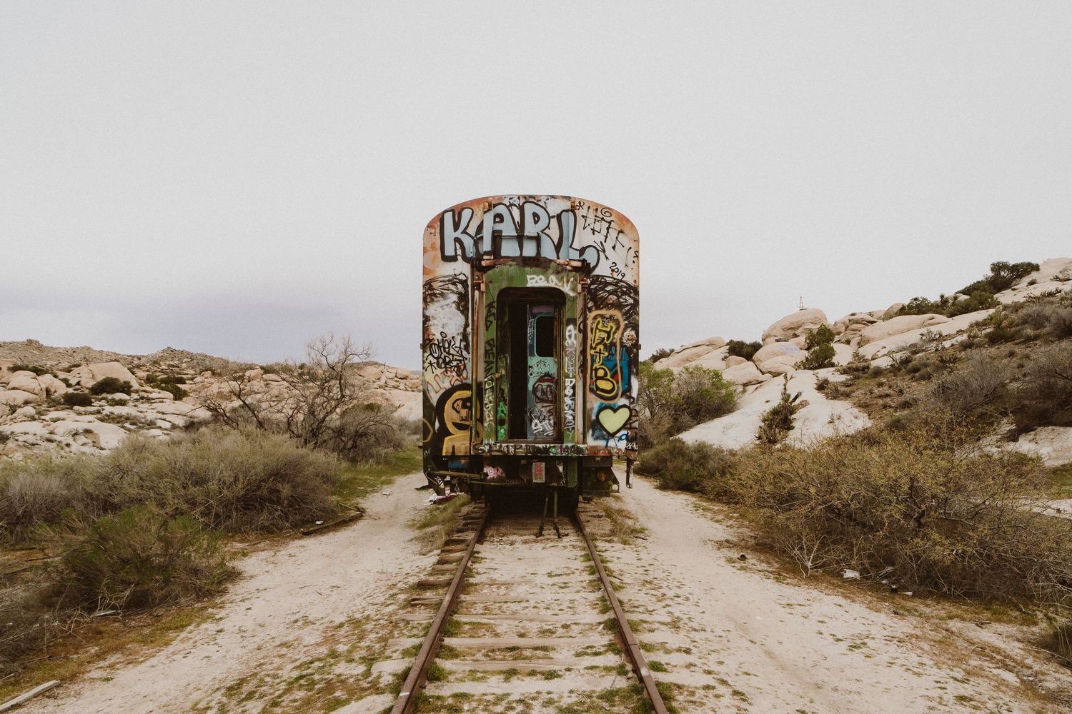 Vintage train cars covered in graffiti sit abandoned on rustic desert tracks against a barren landscape.