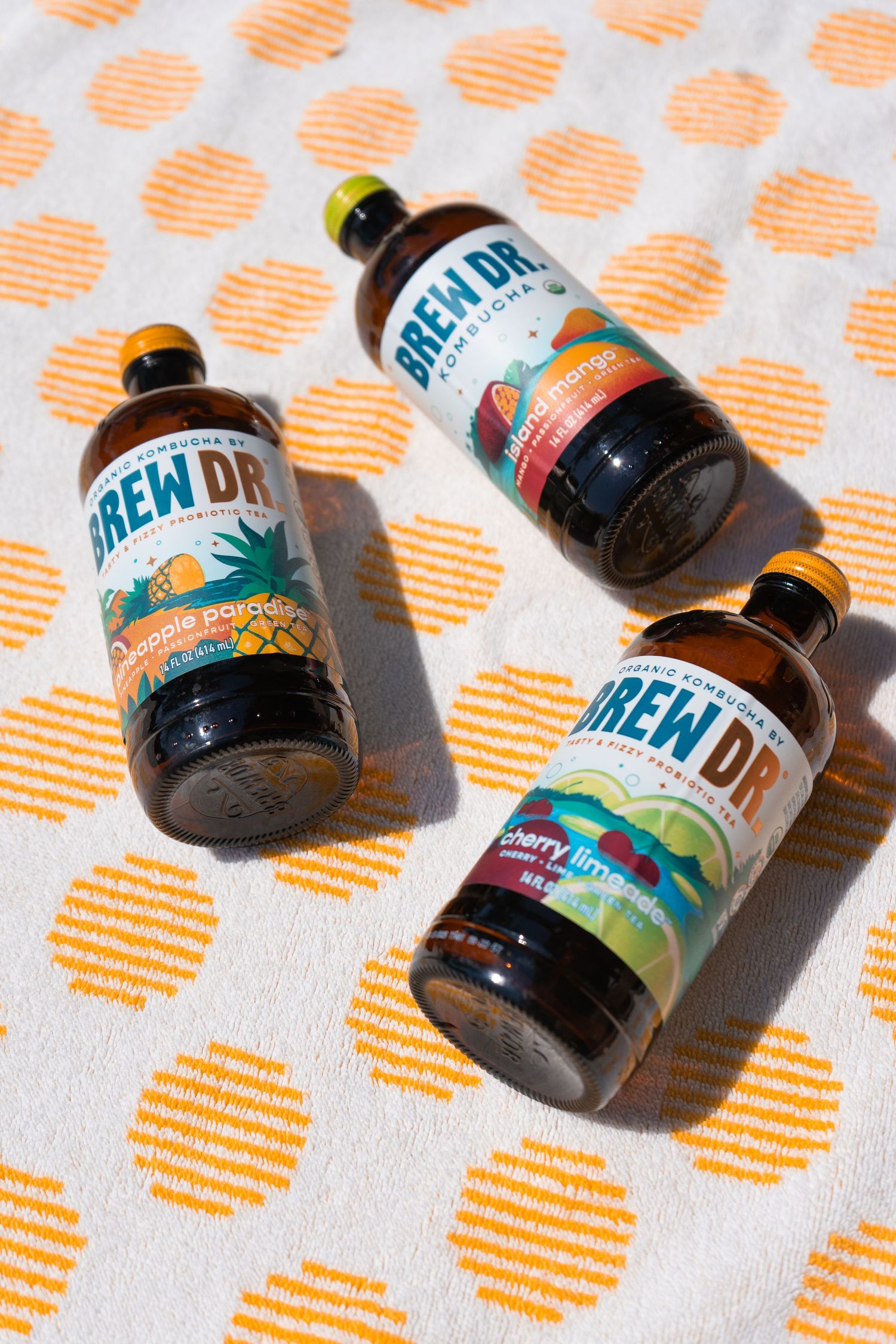 Three Brew Dr. Kombucha bottles arranged on polka dot fabric in bright sunlight.