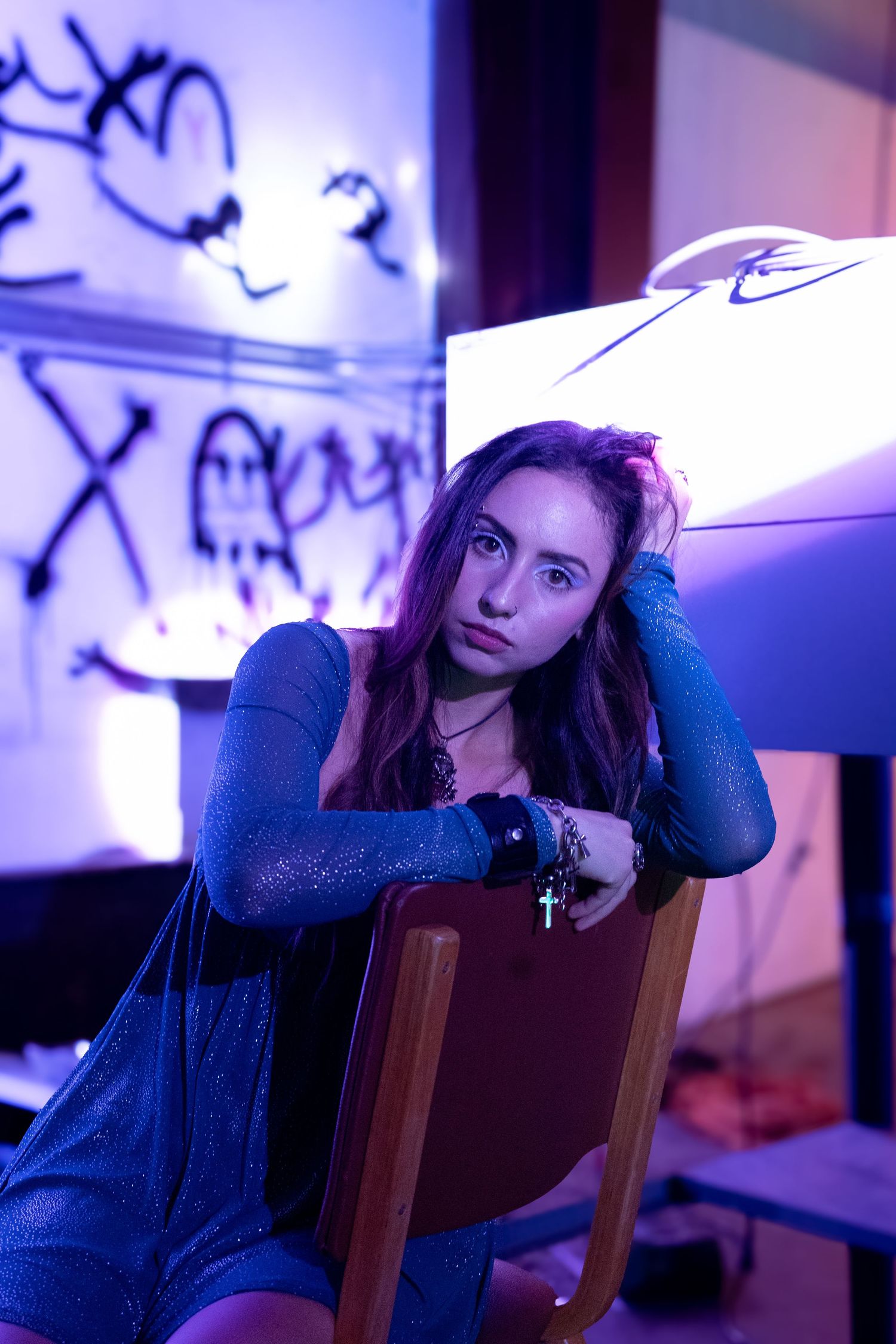 Moody portrait in blue lighting with wooden chairs and artistic background.