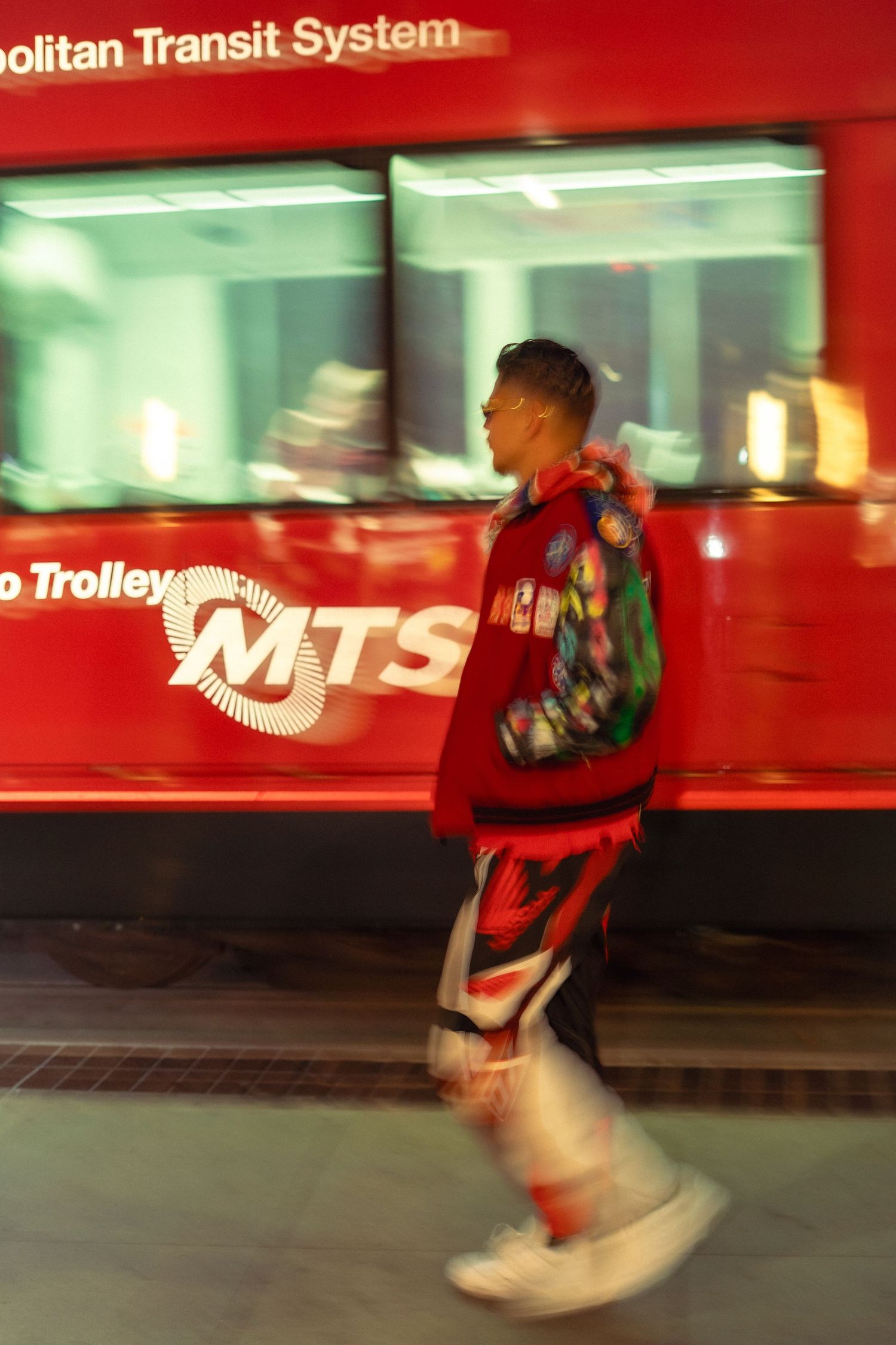 Motion-blurred photo of someone walking past a red Metropolitan Transit System trolley.