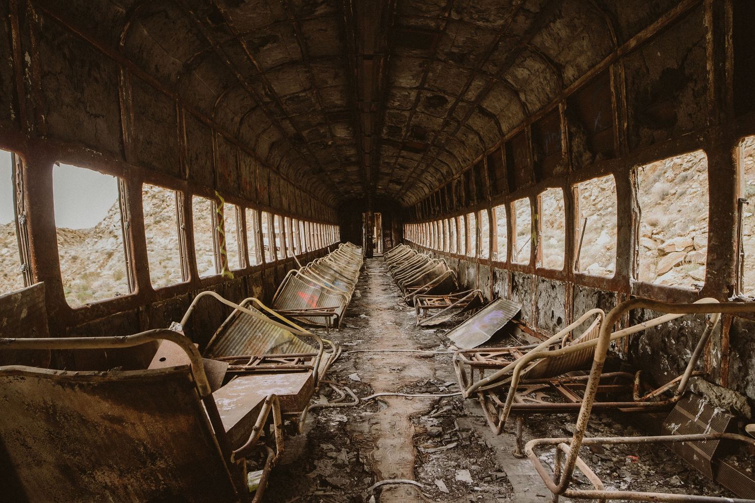 Abandoned train car interior with decaying seats and debris creating an eerie, atmospheric corridor perspective.