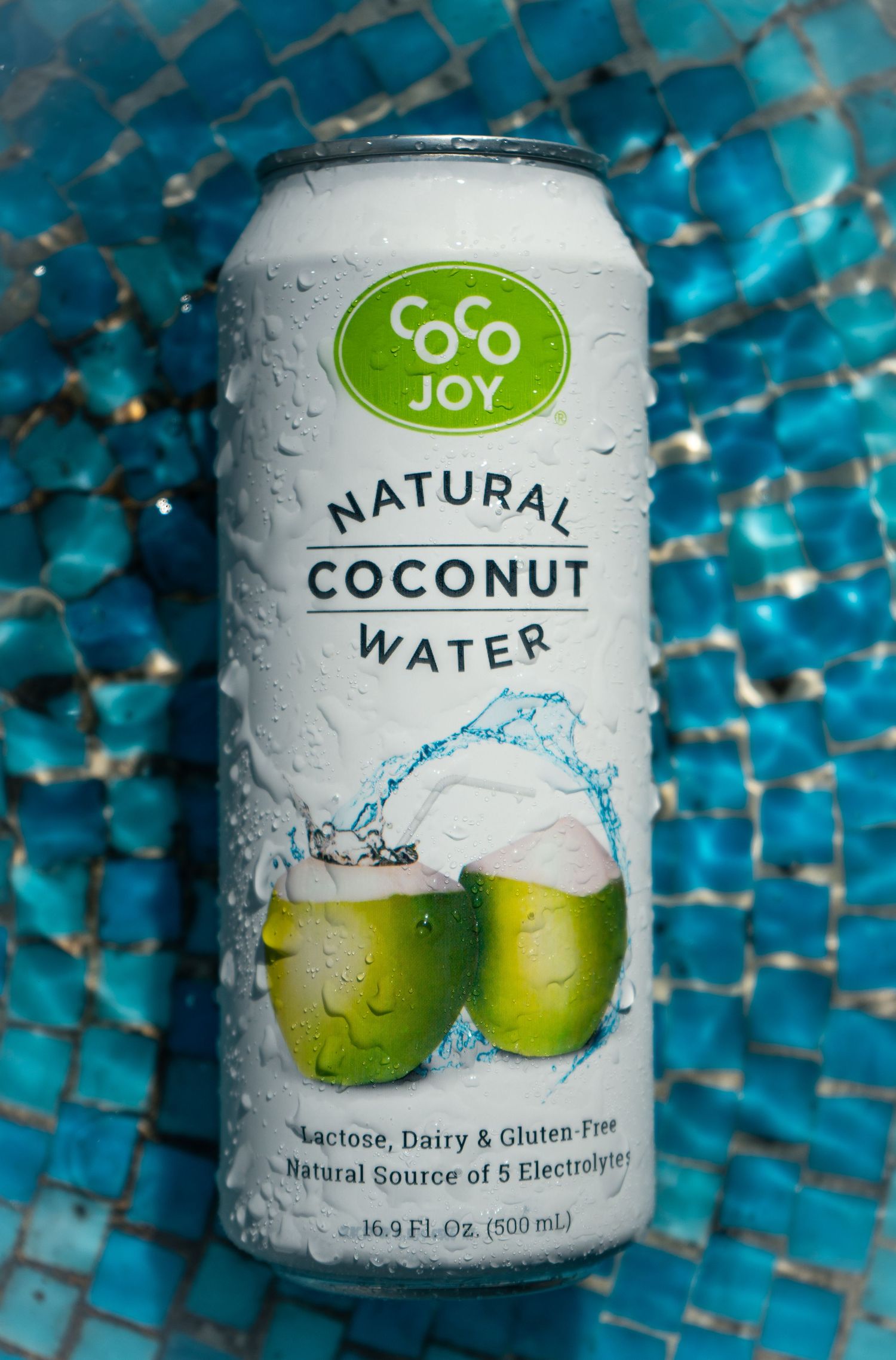A can of Coco Joy natural coconut water with condensation drops against a blue mosaic background.