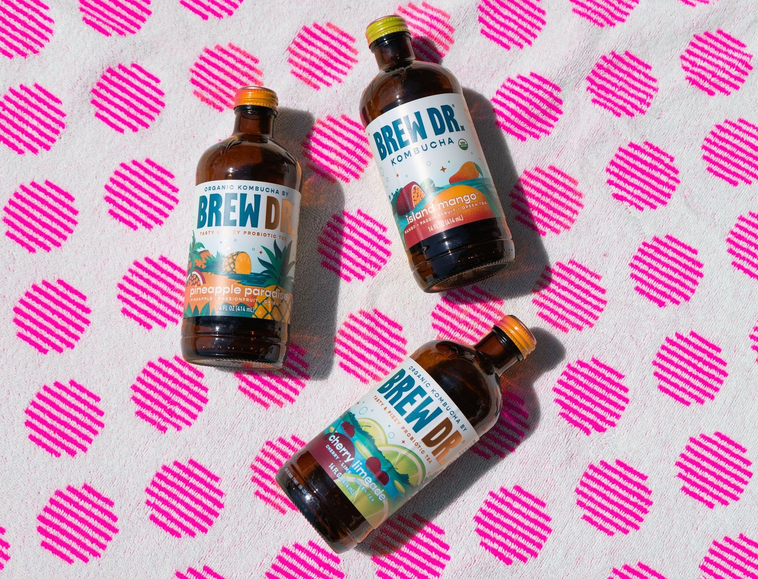 Multiple Brew Dr. Kombucha bottles arranged on pink polka dot patterned background.