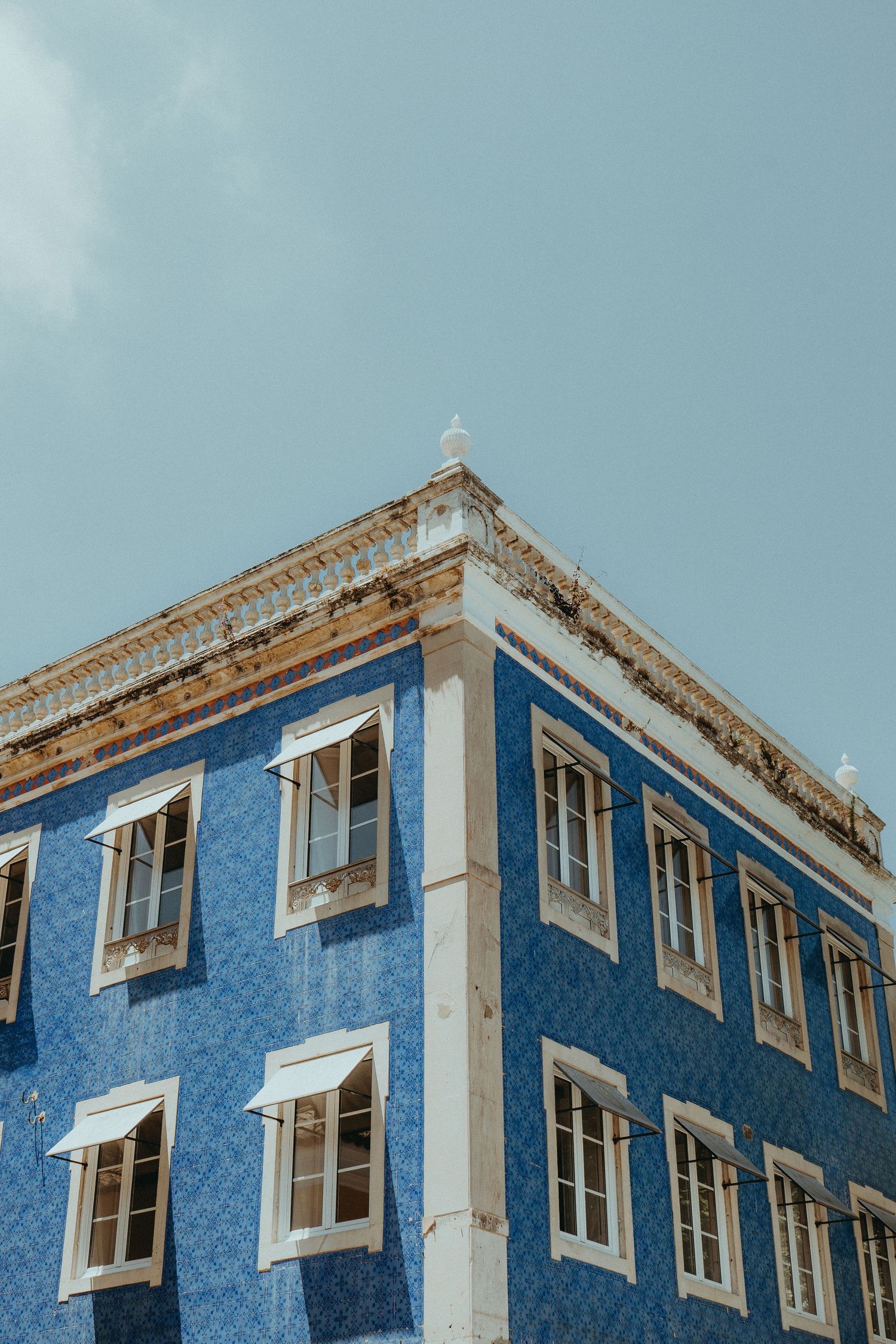 Fragment of bright blue tiled apartment building with white windows and awnings against a clear sky.