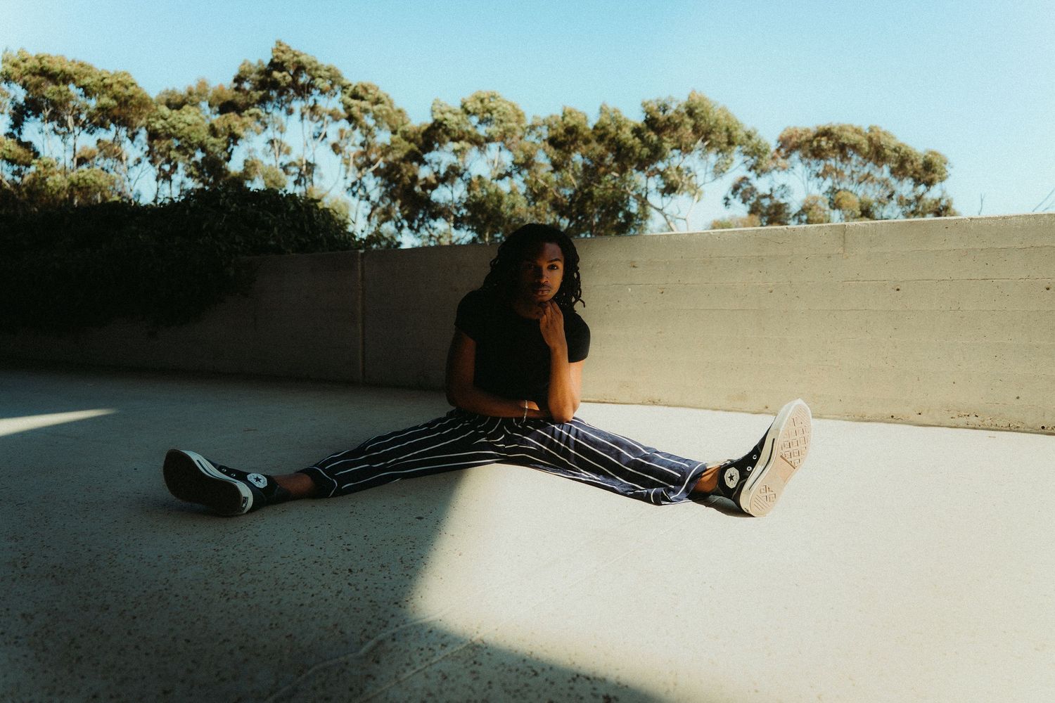 A person sits in a full split pose on a concrete surface with dramatic lighting and shadows during a brand and lifestyle photoshoot in SD