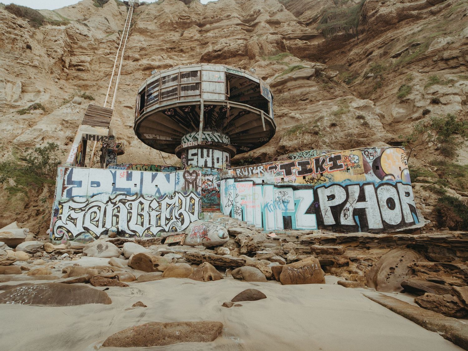 Graffiti art covers rocky cliffs along a desert landscape with scattered boulders in the foreground.