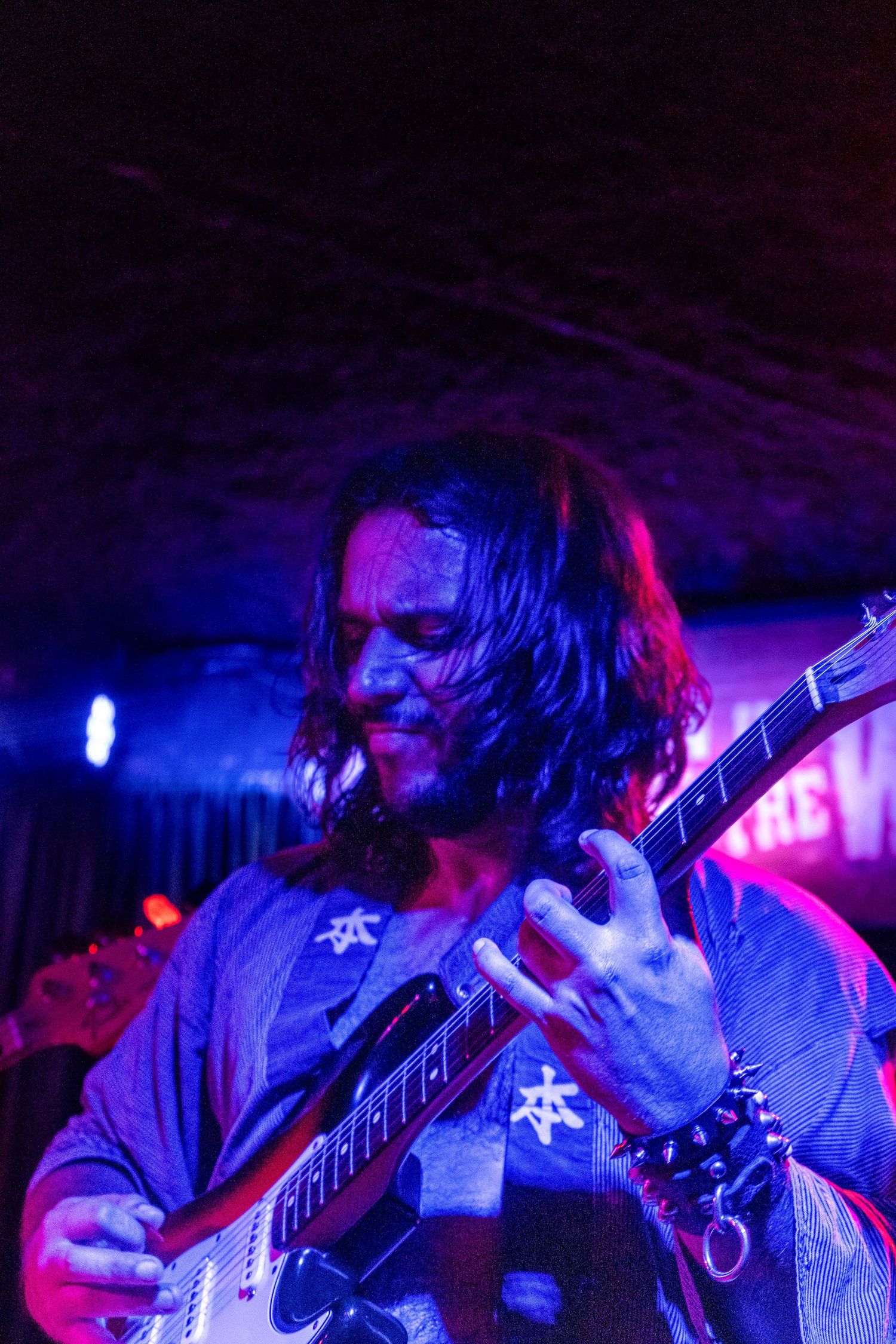 Musicians perform on stage illuminated by vibrant blue and pink lighting at a live concert venue.