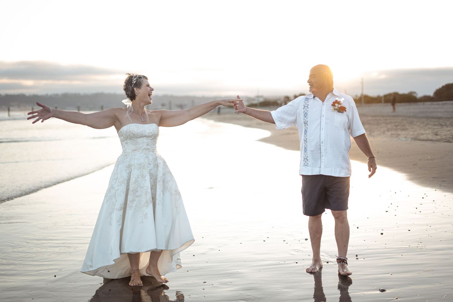 A couple in casual attire walks together on a sandy beach at sunset holding hands.