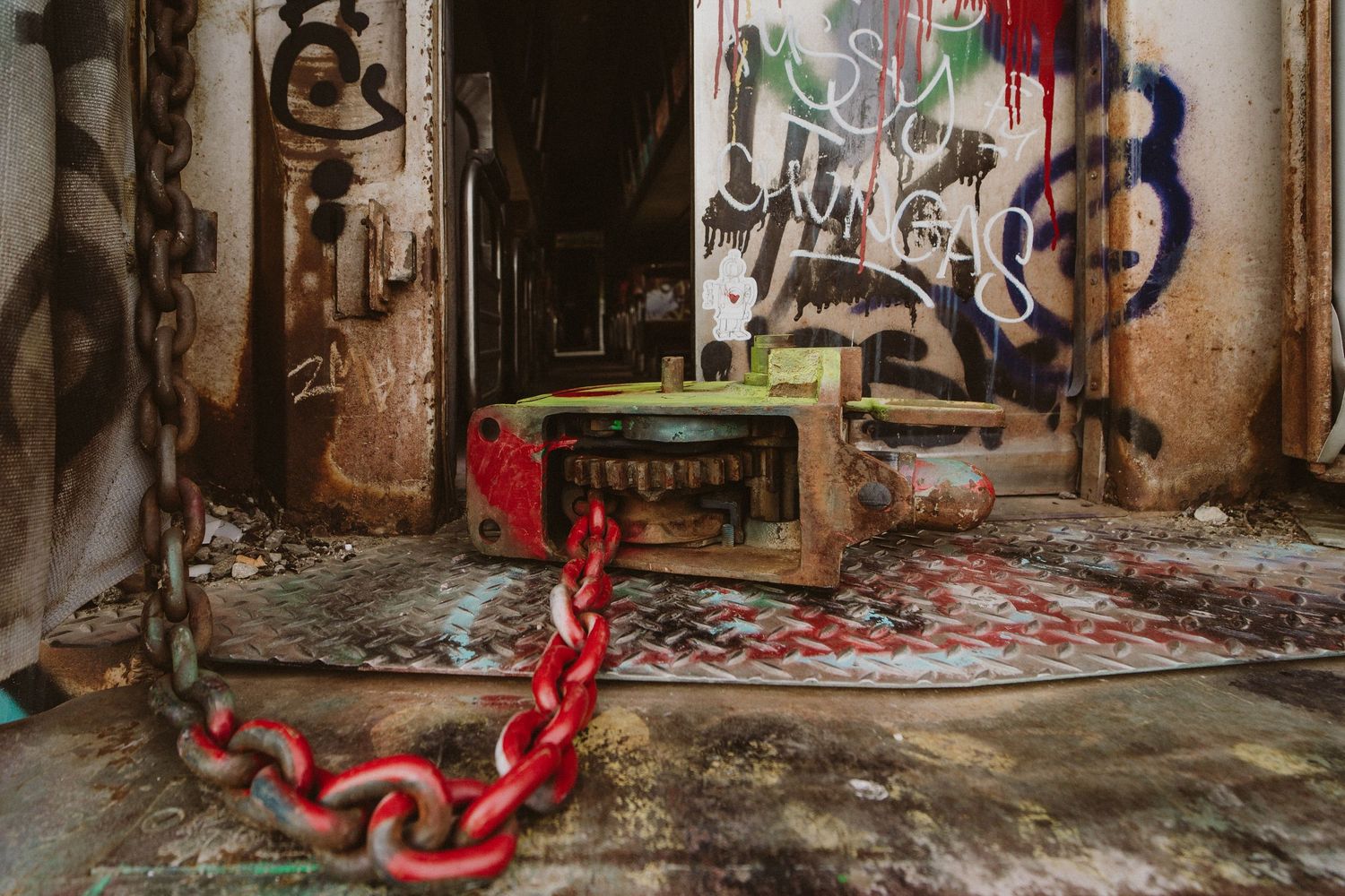 A red metal chain lies on a grungy floor with graffiti-covered walls in an abandoned building.