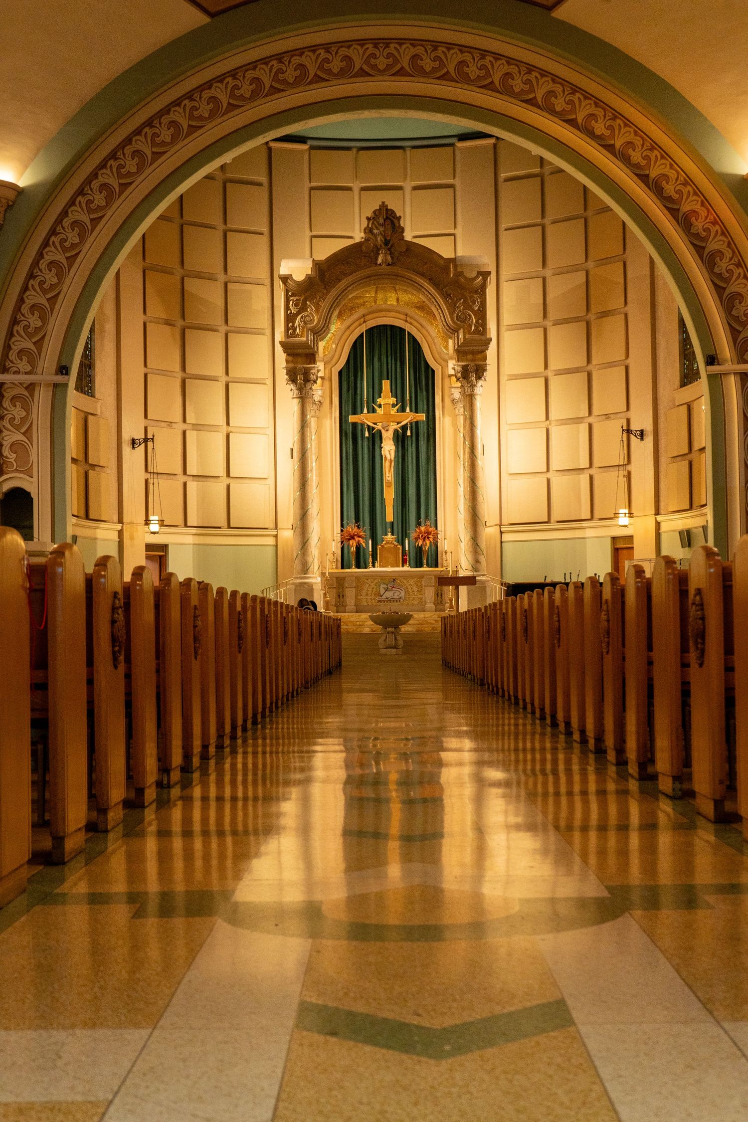 Long symmetrical church aisle with wooden pews and green doors at altar.