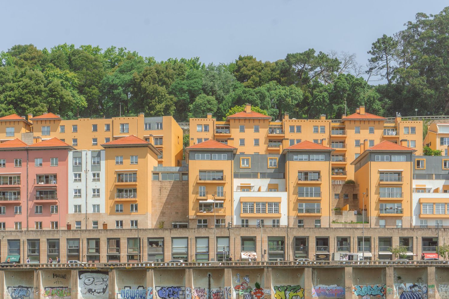 Colorful waterfront buildings with orange and pink facades line a coastal harbor on a sunny day.