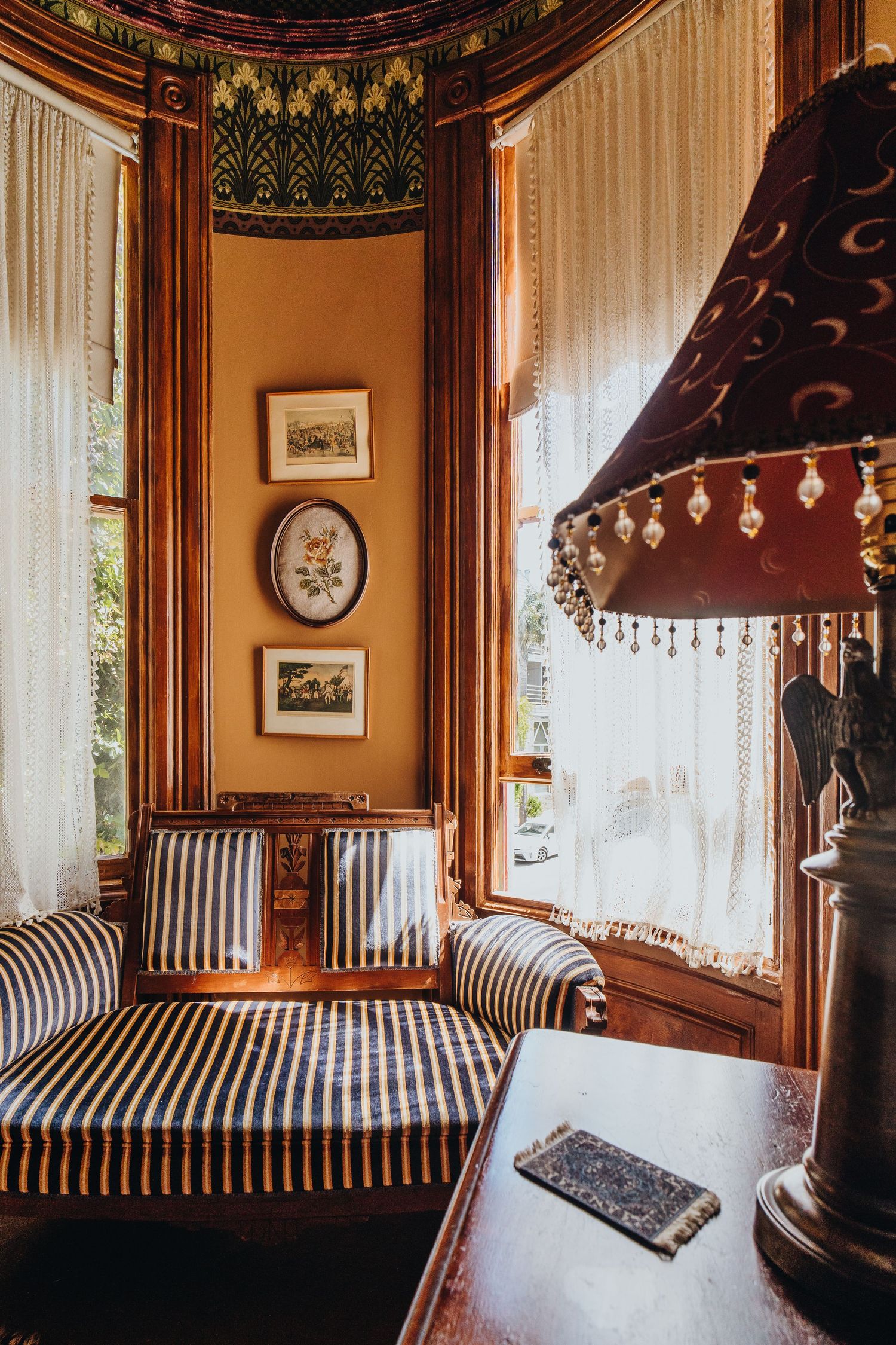 Victorian style sitting nook with striped upholstery, ornate woodwork, and vintage decor in warm lighting.