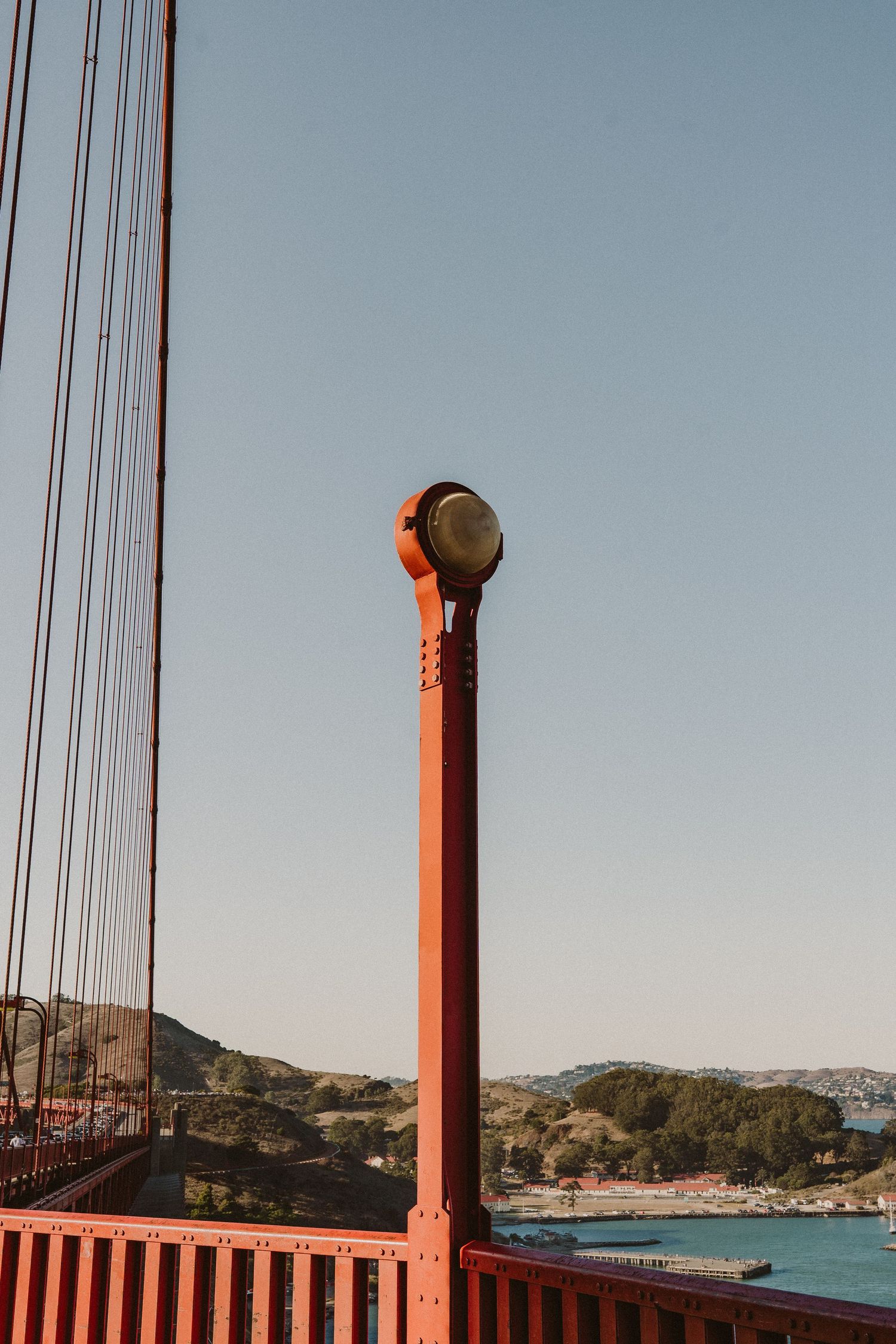 Red metal poles and suspension cables of the Golden Gate Bridge frame a view of San Francisco Bay on a sunny day.