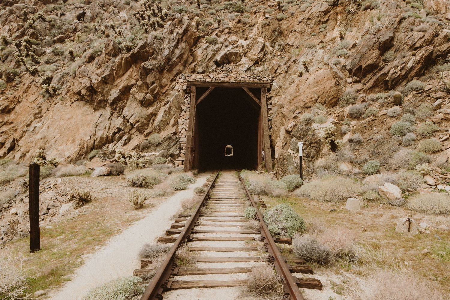A series of four connected photos showing an abandoned mine tunnel entrance with old railroad tracks and stone steps.