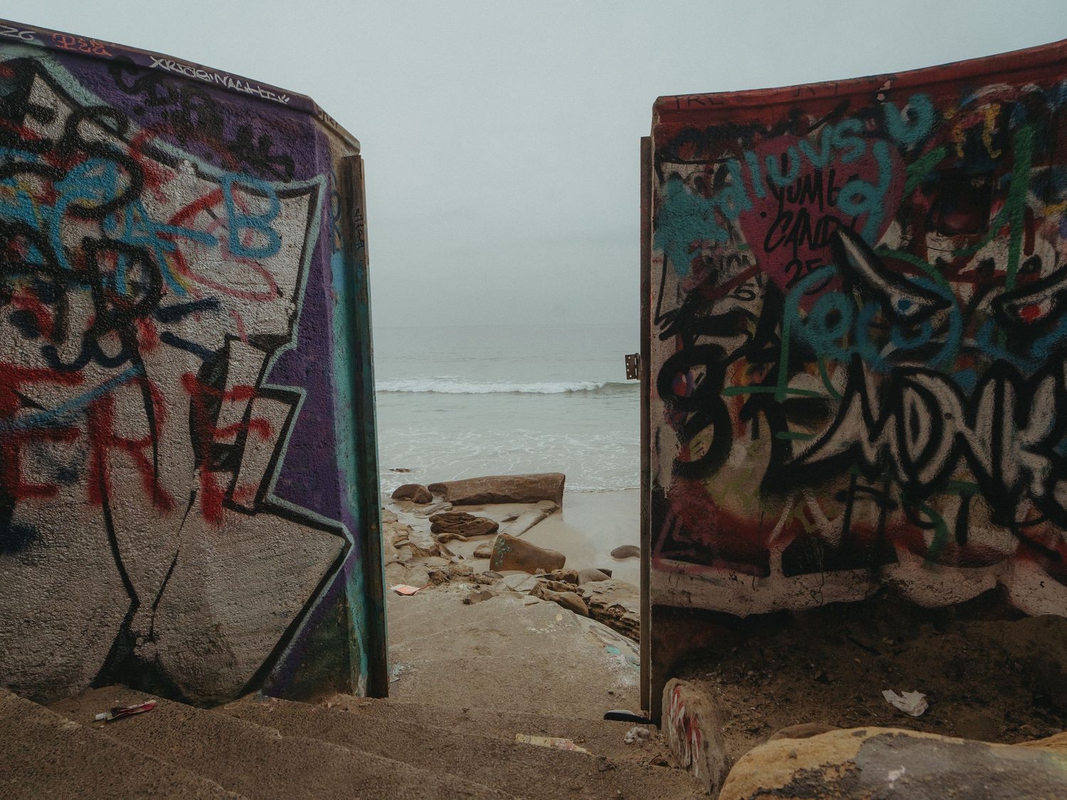 Colorful graffiti art covers a series of metal barriers along a beach shoreline at sunset.