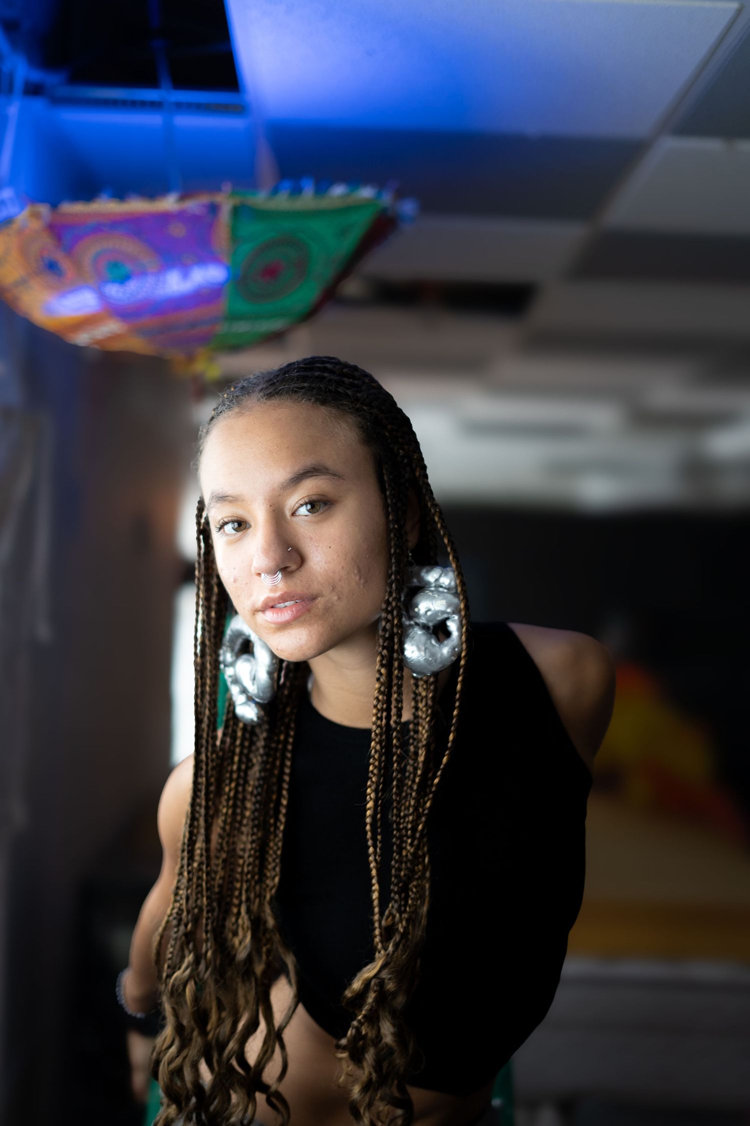 Portrait featuring braided hair and statement earrings against dark background with colorful lighting.