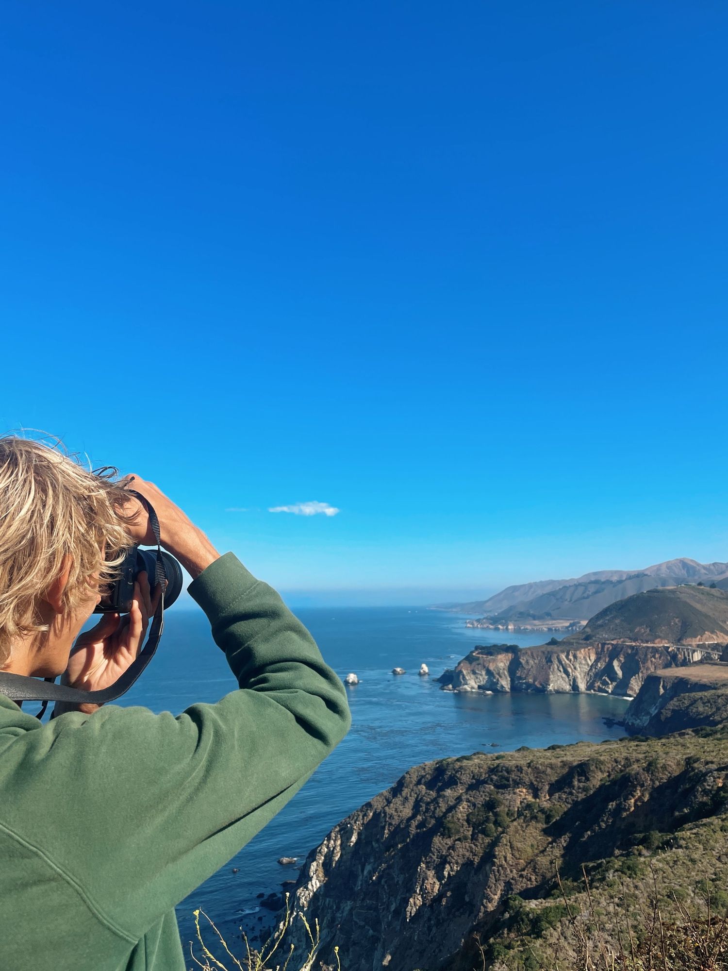 Someone observes the rugged California coastline and cliffs along Muir Beach Overlook on a clear sunny day with blue skies.