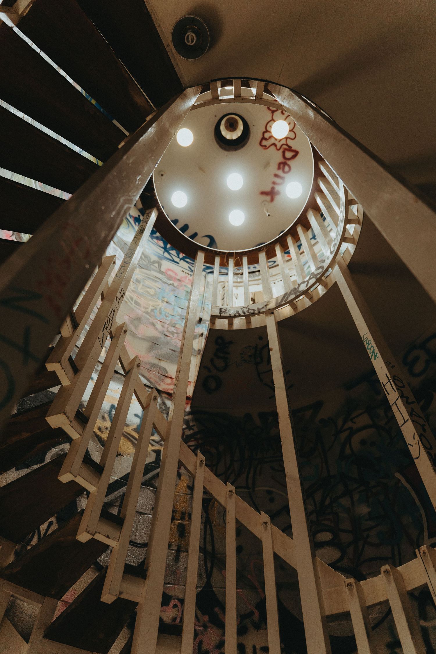 Looking up through a spiral staircase with wooden beams and circular skylight creating dramatic architectural lines.